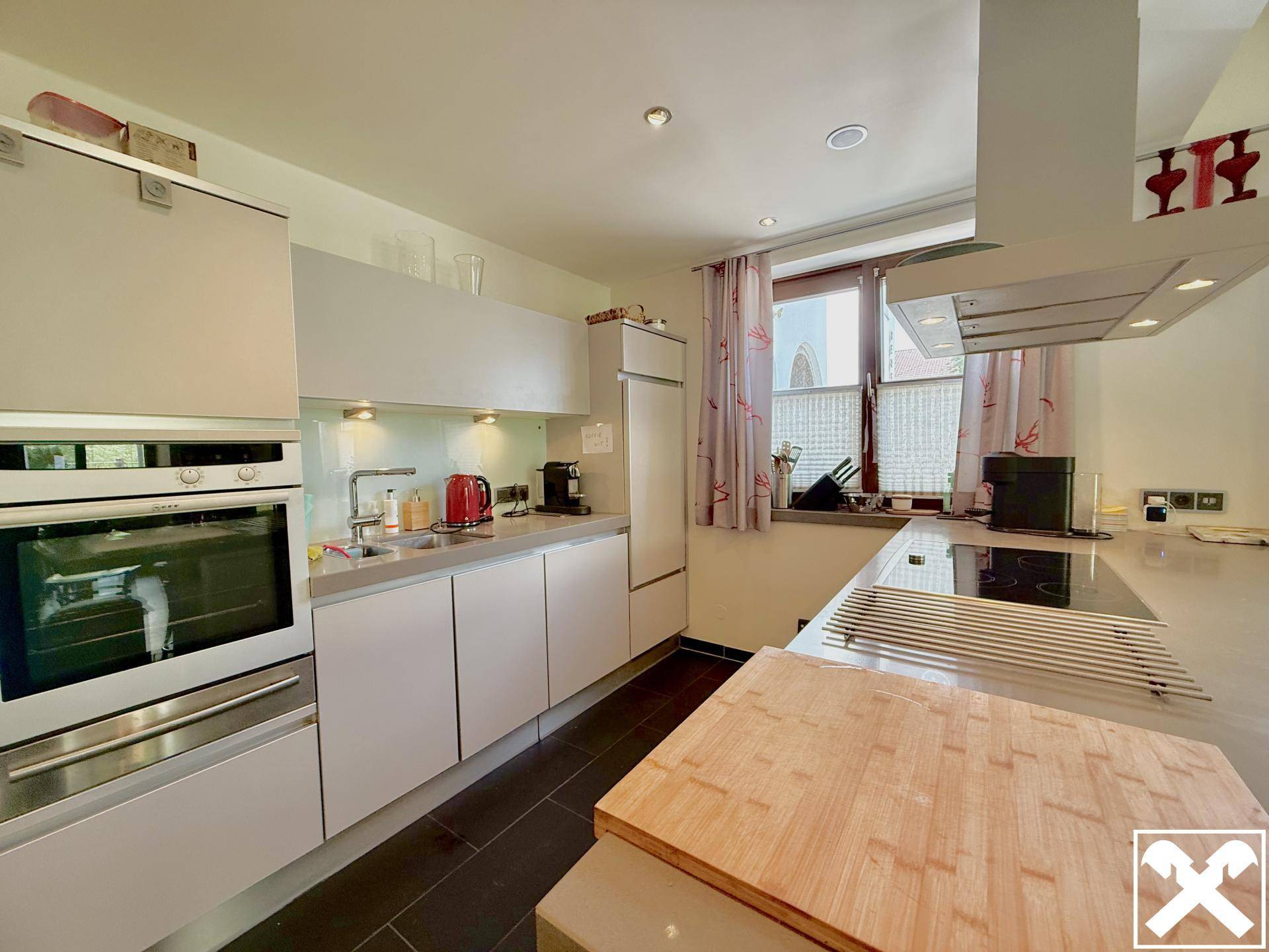 Moderne Küche mit hellgrauen Schränken, integriertem Backofen und Induktionskochfeld.