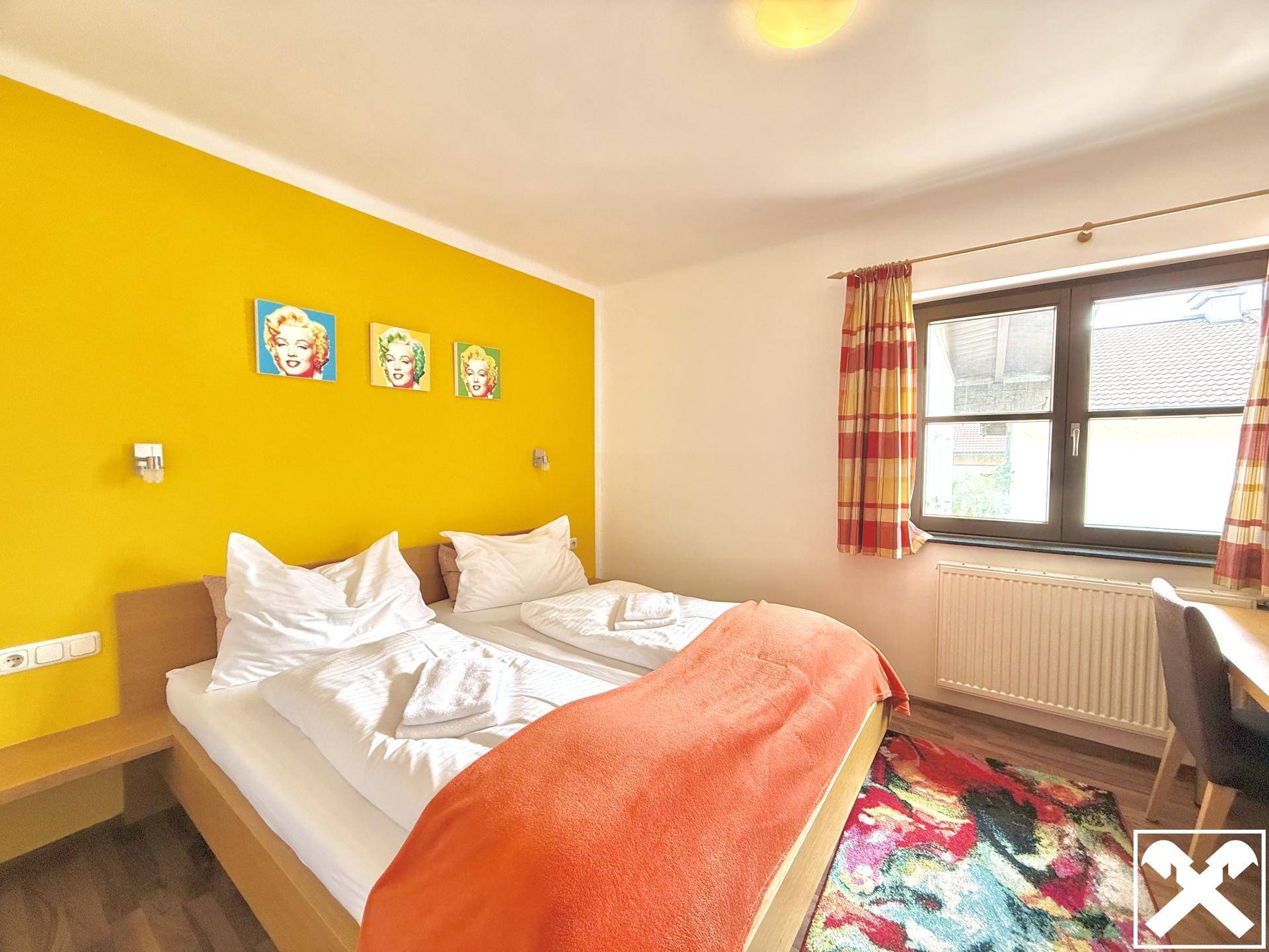 Schlafzimmer mit zwei Einzelbetten, einer leuchtend gelben Wand und Fenster.