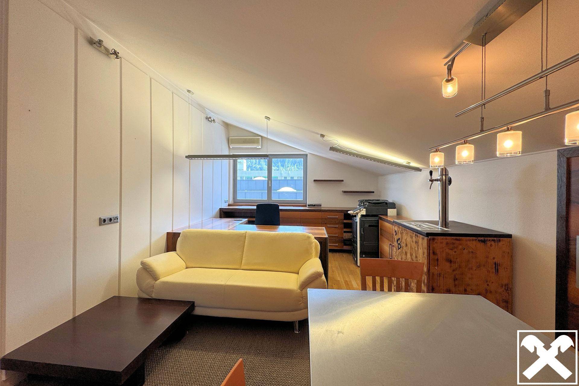 Gemütlicher Dachgeschossraum mit schräger Decke, Sofa und einer kleinen Bar, ideal als Aufenthaltsbereich.