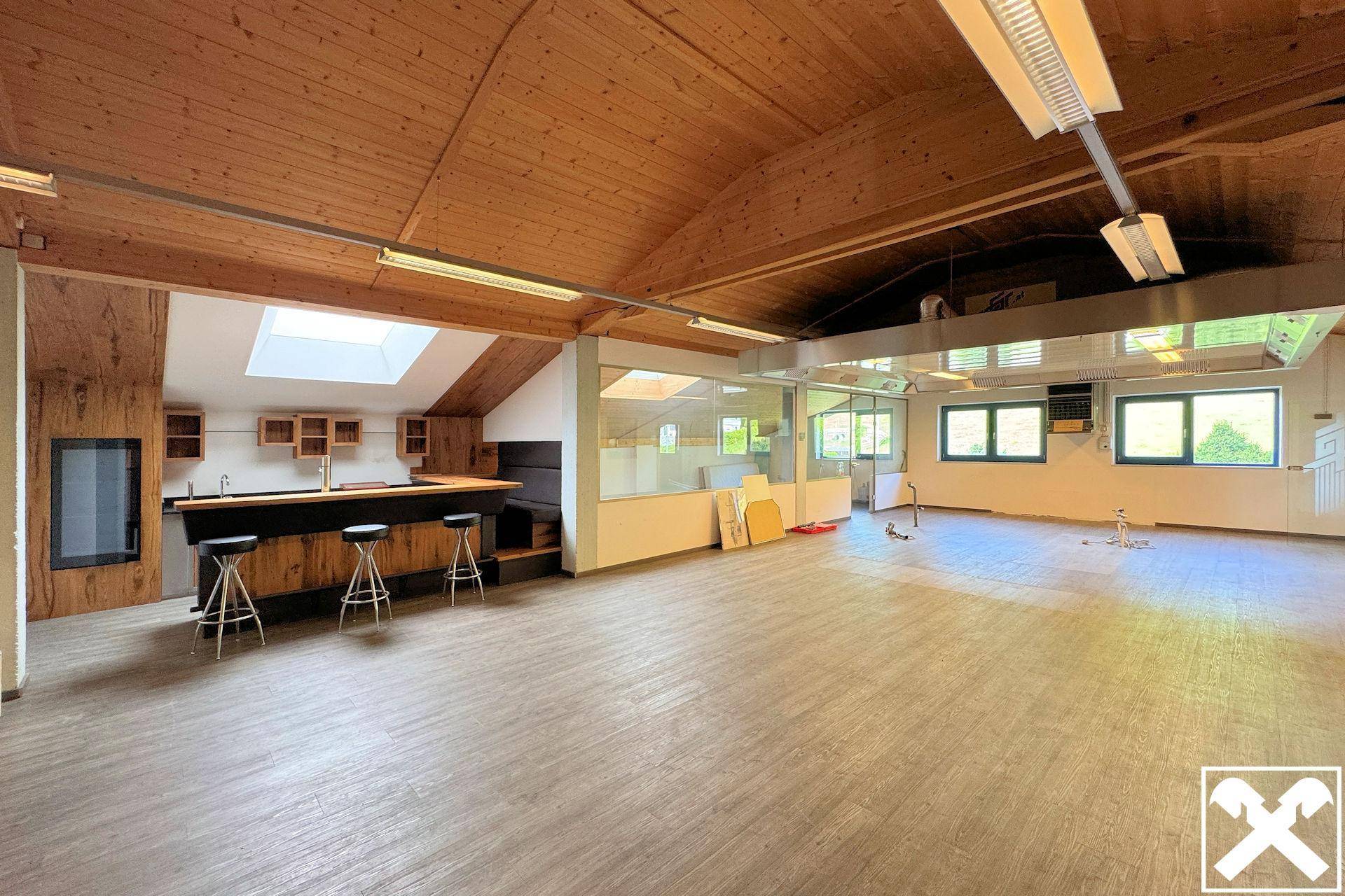 Weitläufiger Gewerberaum mit Holzdecke, Vinylboden und einer voll ausgestatteten Bar mit Hockern.