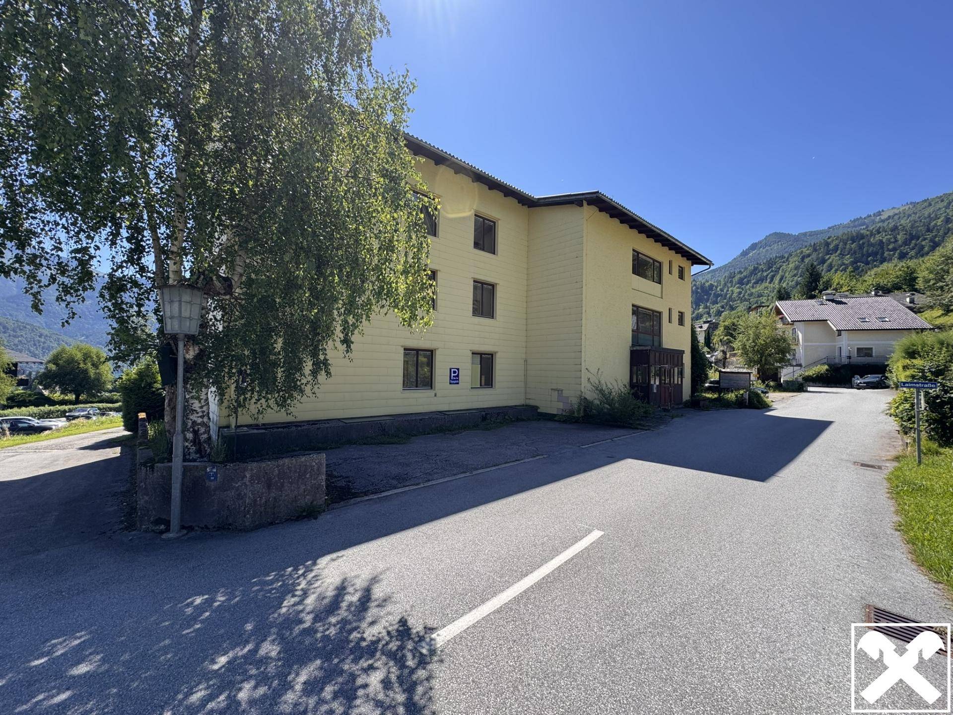 Seitenansicht des Gebäudes mit Parkplätzen und Zufahrtsstraße, umgeben von grünen Hügeln.