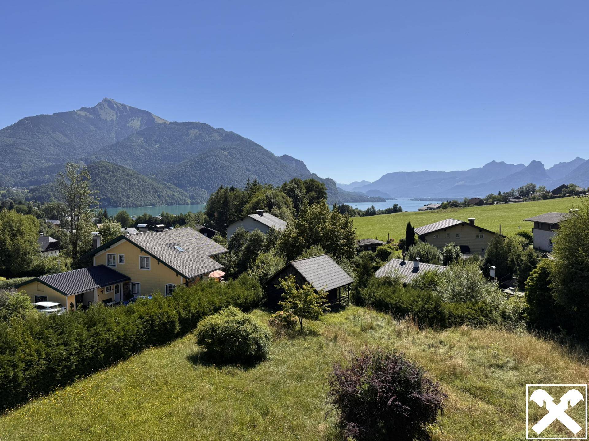 Panoramablick über eine Siedlung mit Häusern, einem See und majestätischen Bergen im Hintergrund.