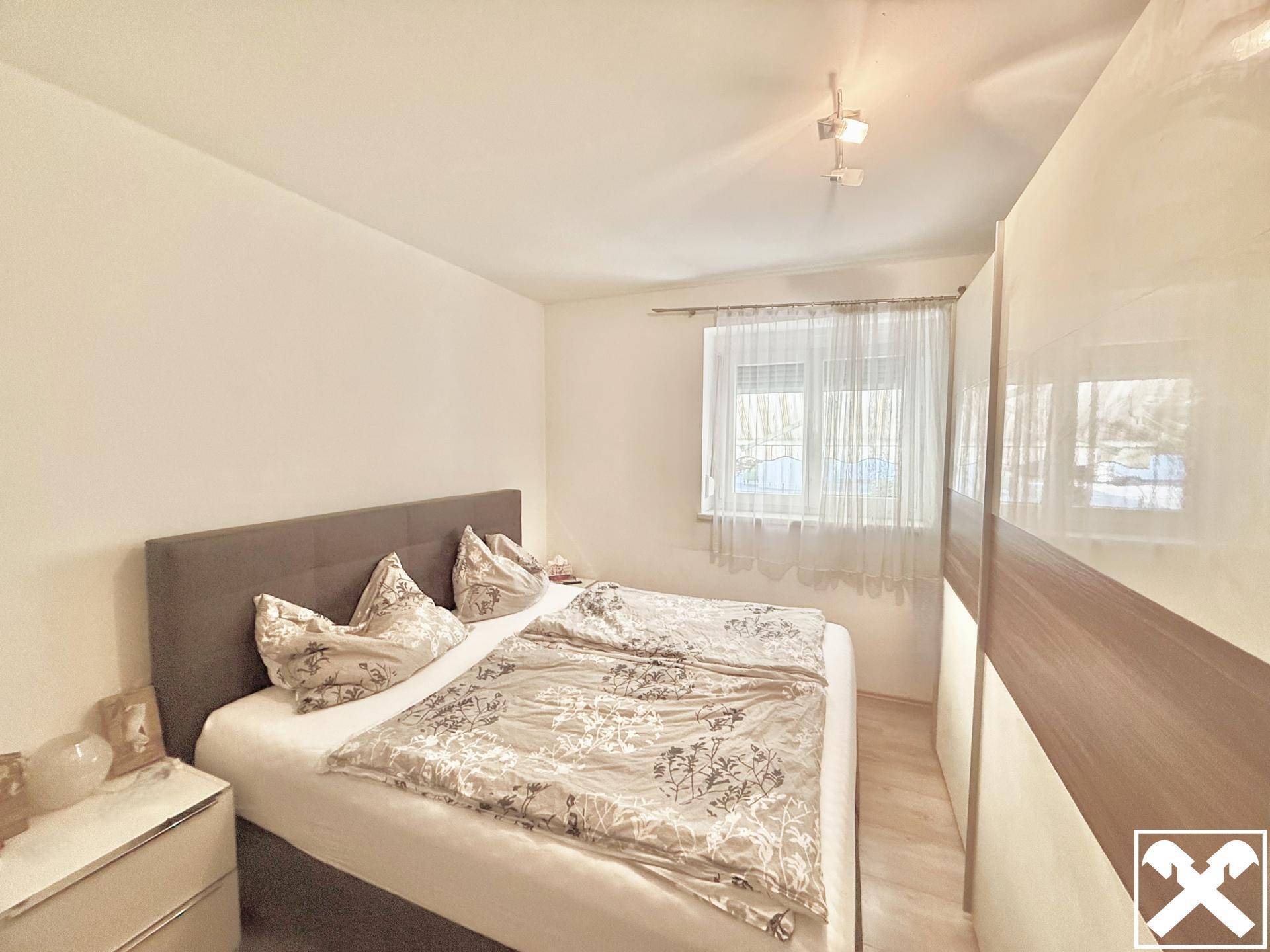Schlafzimmer mit Doppelbett, Einbauschrank und Laminatboden, hell durch Tageslicht.