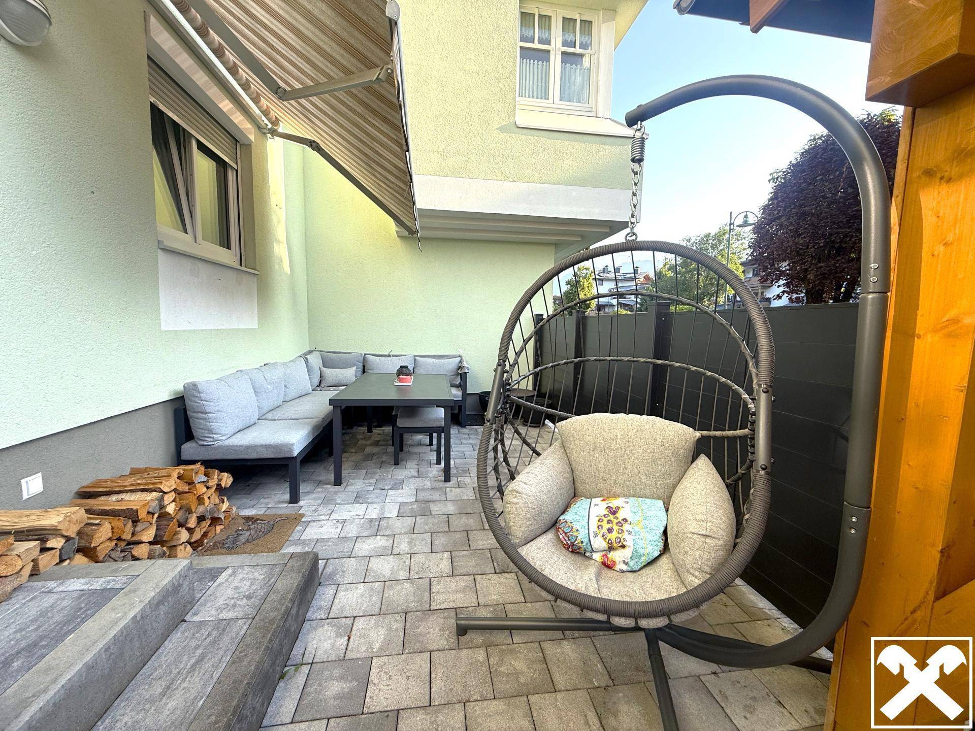 Gemütliche Terrasse mit Outdoor-Sitzgruppe, Hängesessel und Holzstapel für den Kamin.