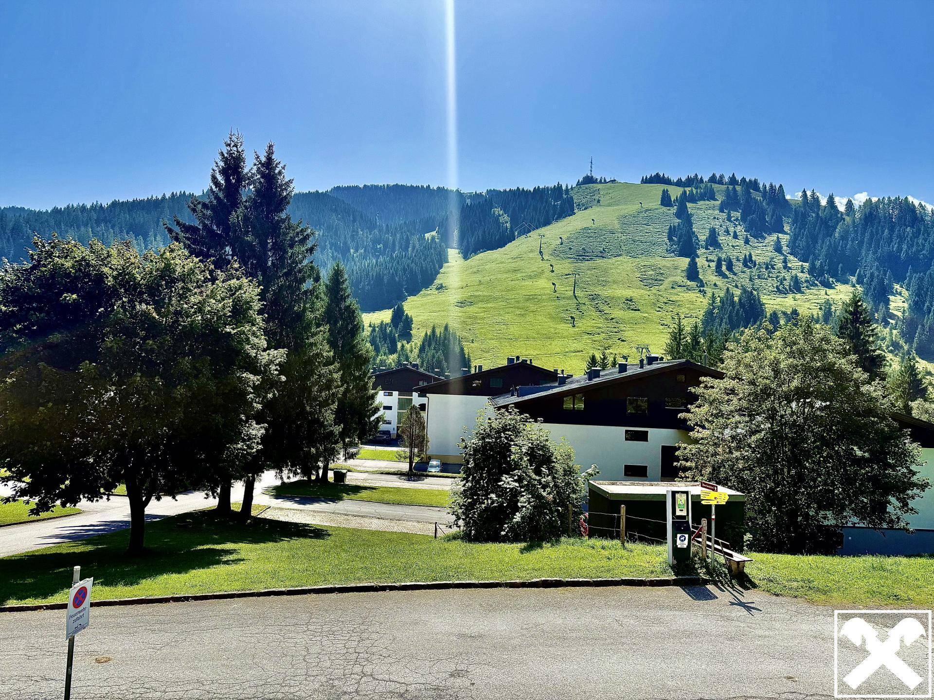 Außenansicht des Gebäudes mit Blick auf die grüne Berglandschaft und Skipisten.