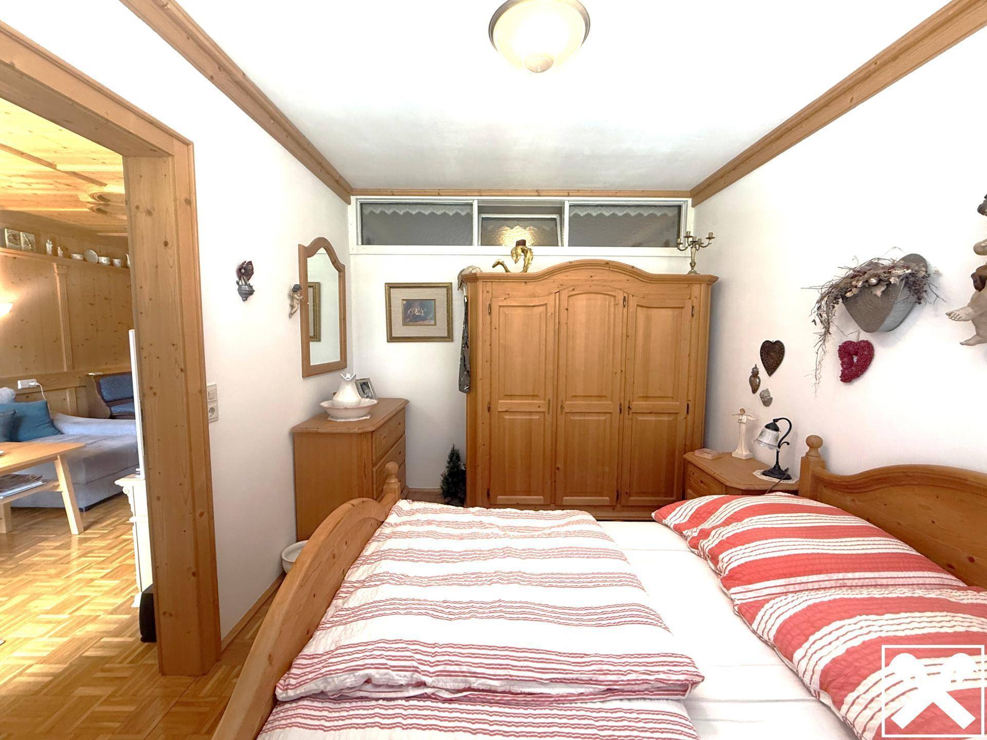 Schlafzimmer mit traditionellen Holzmöbeln, gestreifter Bettwäsche und Zugang zum Wohnbereich.