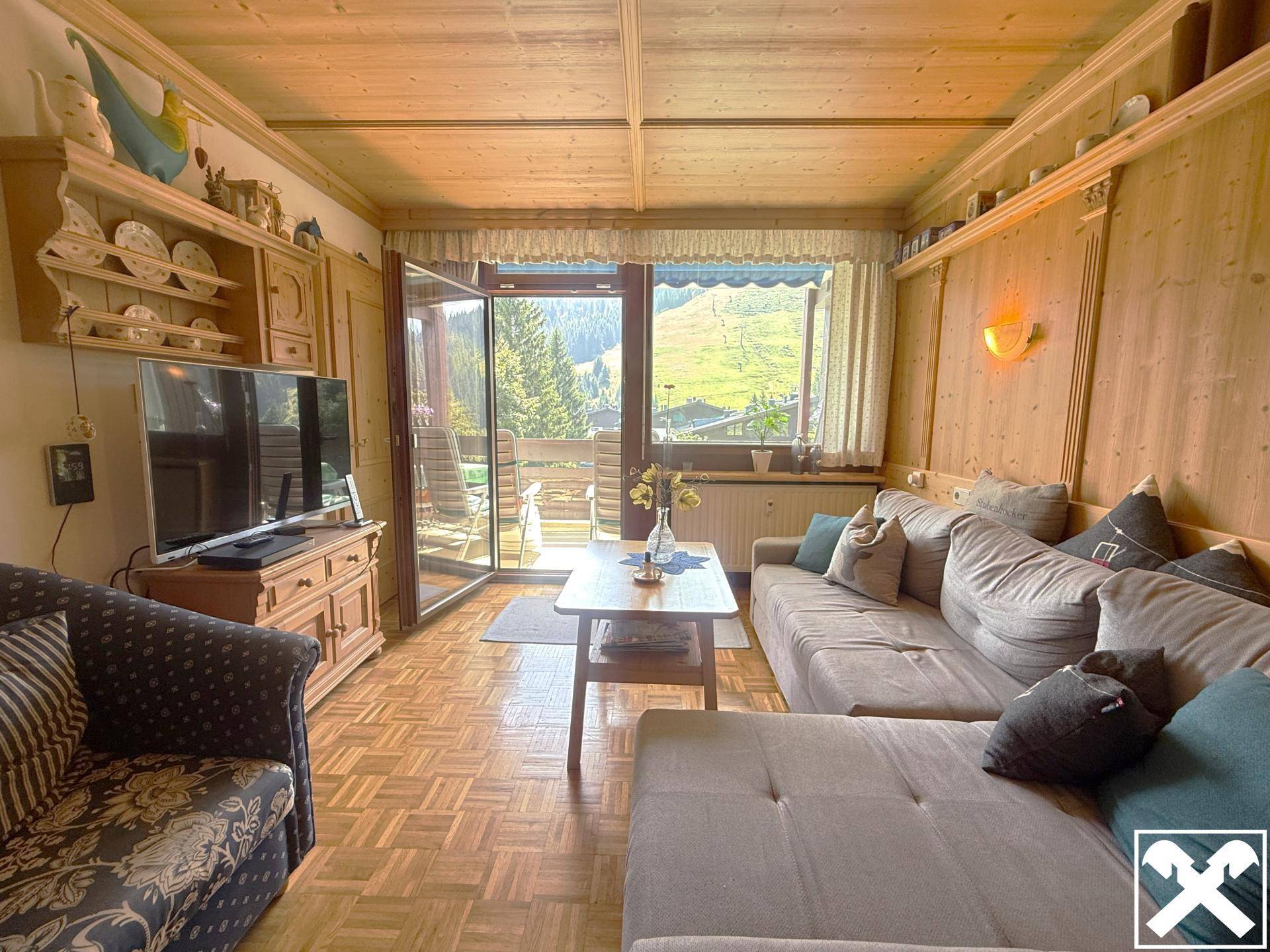 Gemütliches Wohnzimmer mit Sofa, Fernseher und Balkonzugang mit Bergblick.