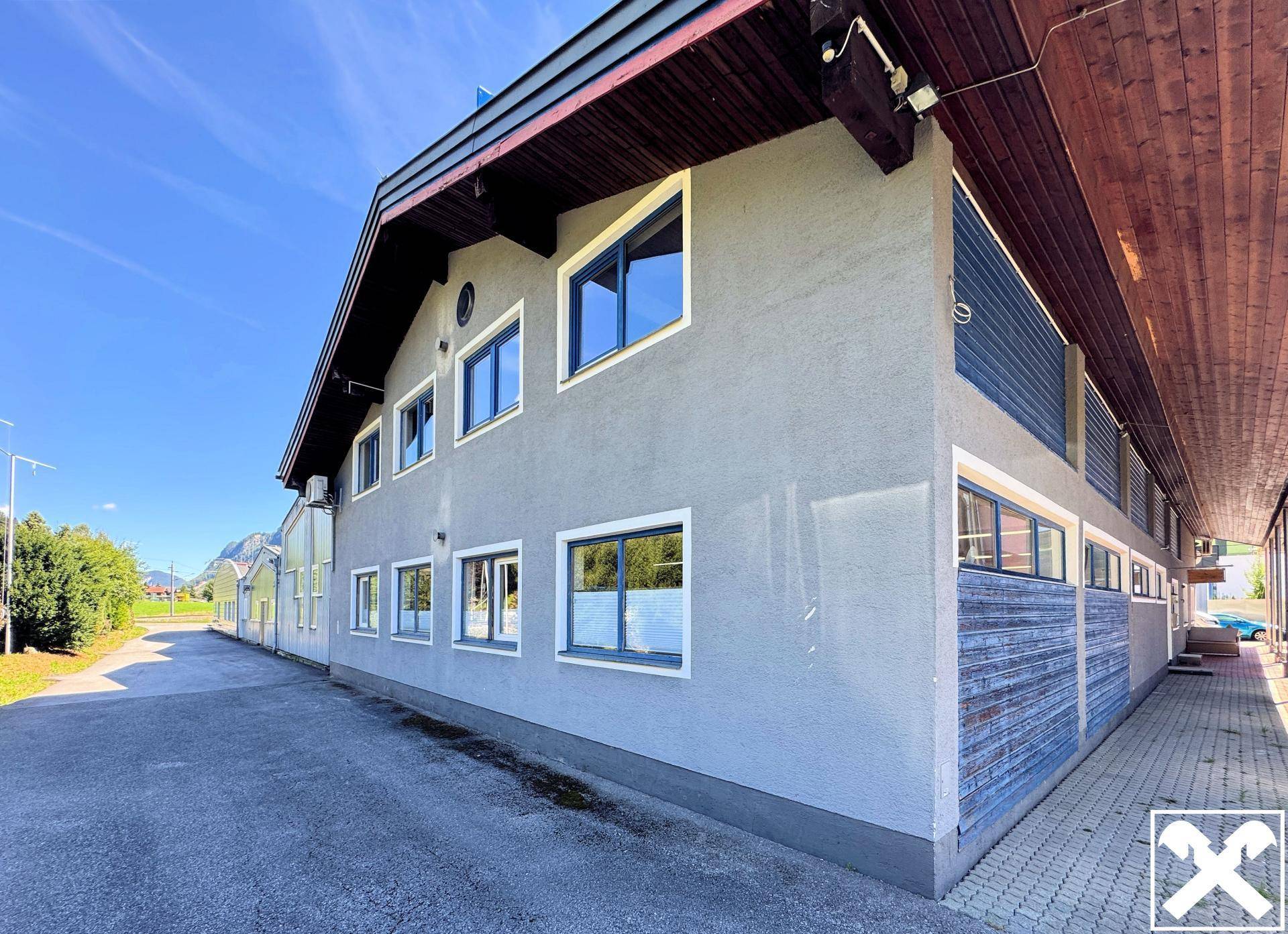 Modernes Gebäude mit grauer Fassade, dunklen Fenstern und Holzelementen unter dem Dach.