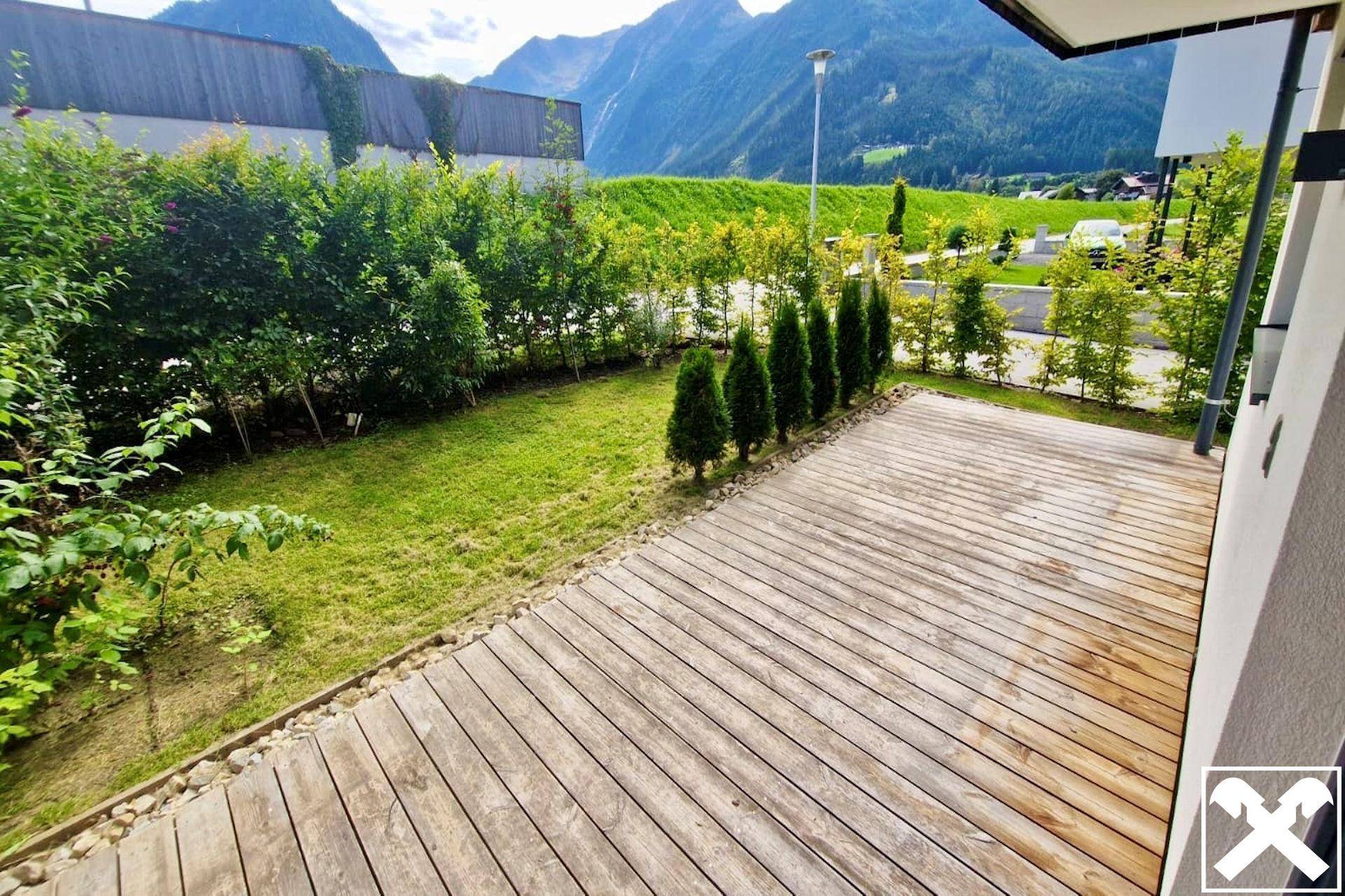 Geräumige Holzterrasse mit angrenzendem Rasen und Blick auf die umliegende Berglandschaft.