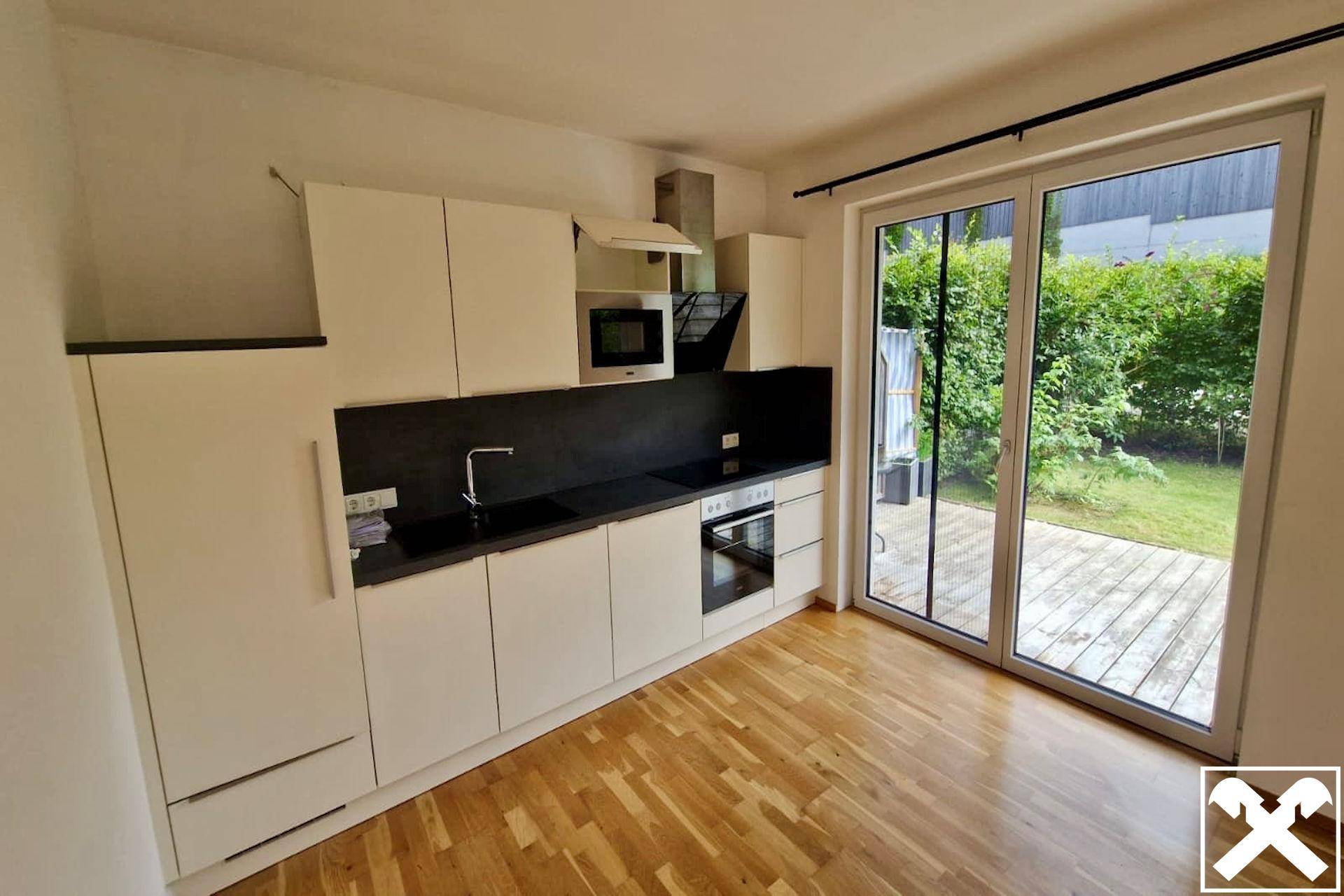 Helle Küche mit modernen weißen Schränken, dunkler Arbeitsplatte und Zugang zur Terrasse.