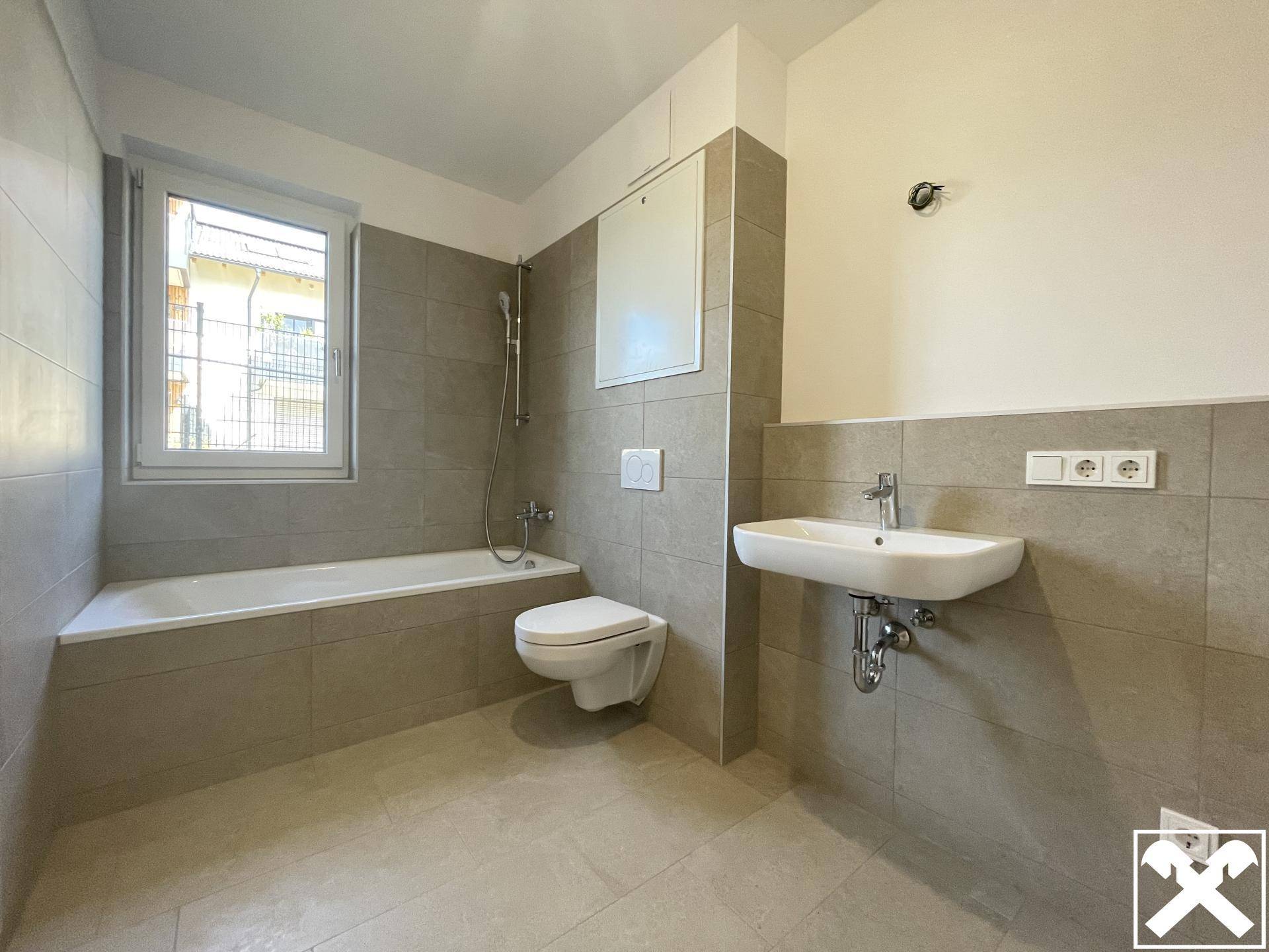 Modernes Badezimmer mit Badewanne, WC, Waschbecken und großen grauen Fliesen.