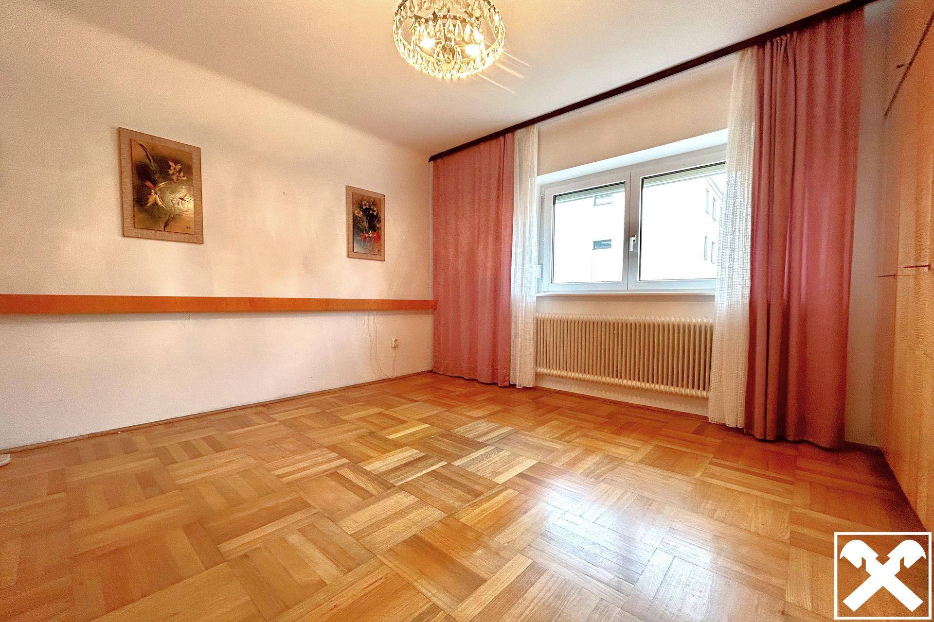 Helles Schlafzimmer mit Parkettboden und großem Fenster, bereit zur individuellen Gestaltung.
