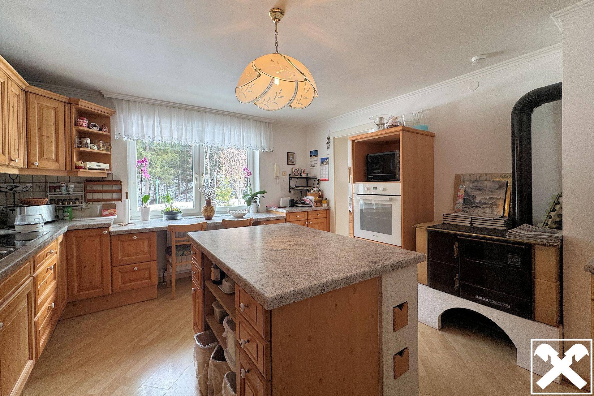 Gemütliche Küche im Landhausstil mit Holzeinbauten, Kücheninsel und traditionellem Holzofen.