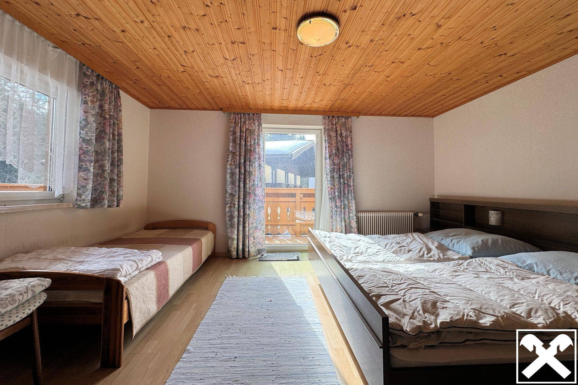 Helles Schlafzimmer mit Holzdecke, zwei Betten und Zugang zu einem kleinen Balkon.