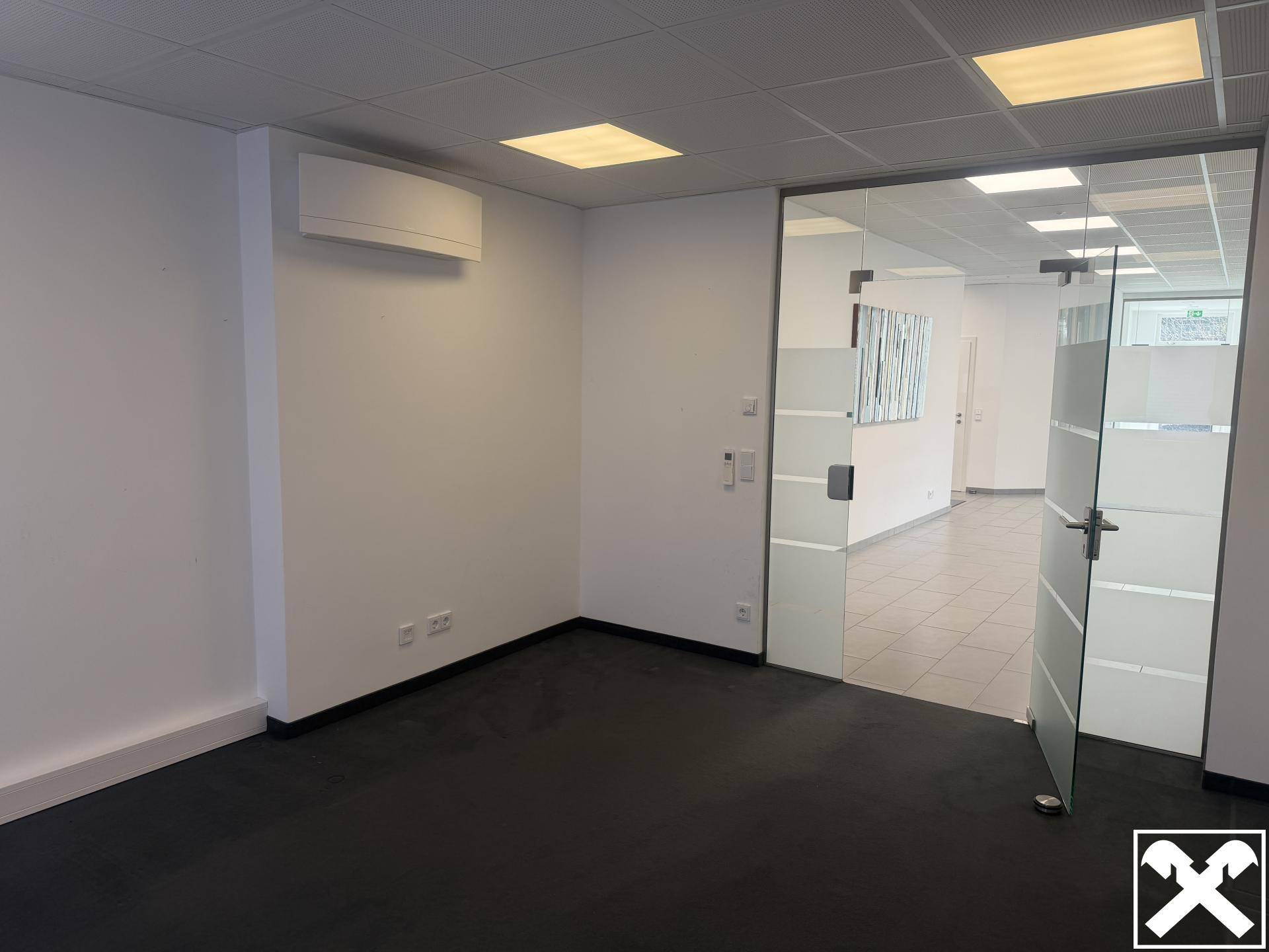 Leeres Büro mit dunklem Boden, Glastür und Klimaanlage an der Wand.