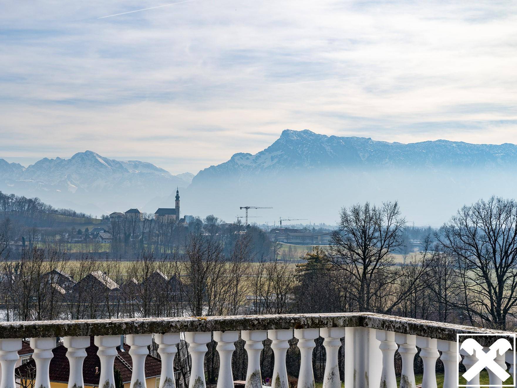 Panoramablick von einem Balkon mit weißer Balustrade über eine Stadt und die beeindruckende Bergkulisse.