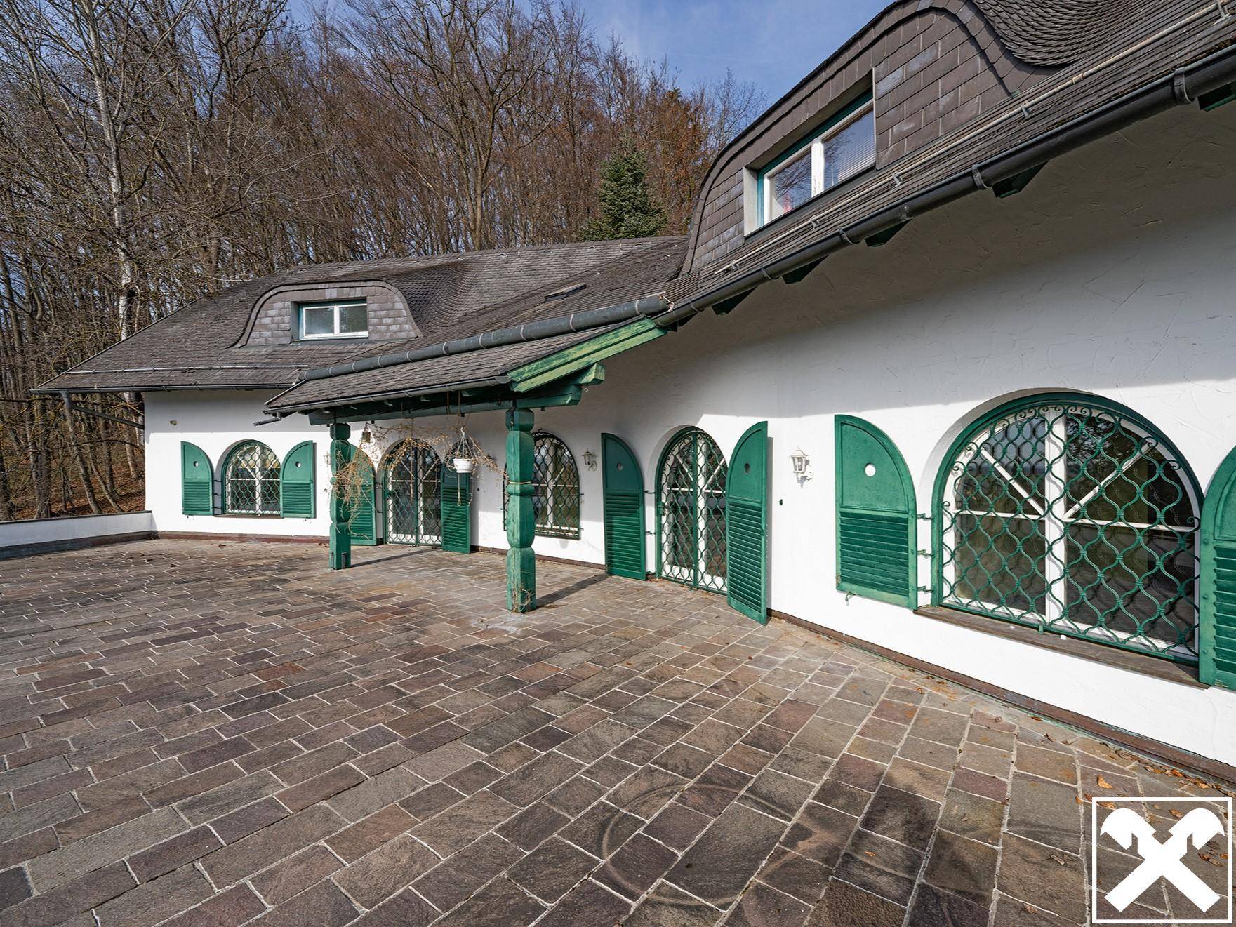 Gepflasterter Außenbereich vor dem Haus mit markanten grünen Fensterläden und überdachtem Eingangsbereich.
