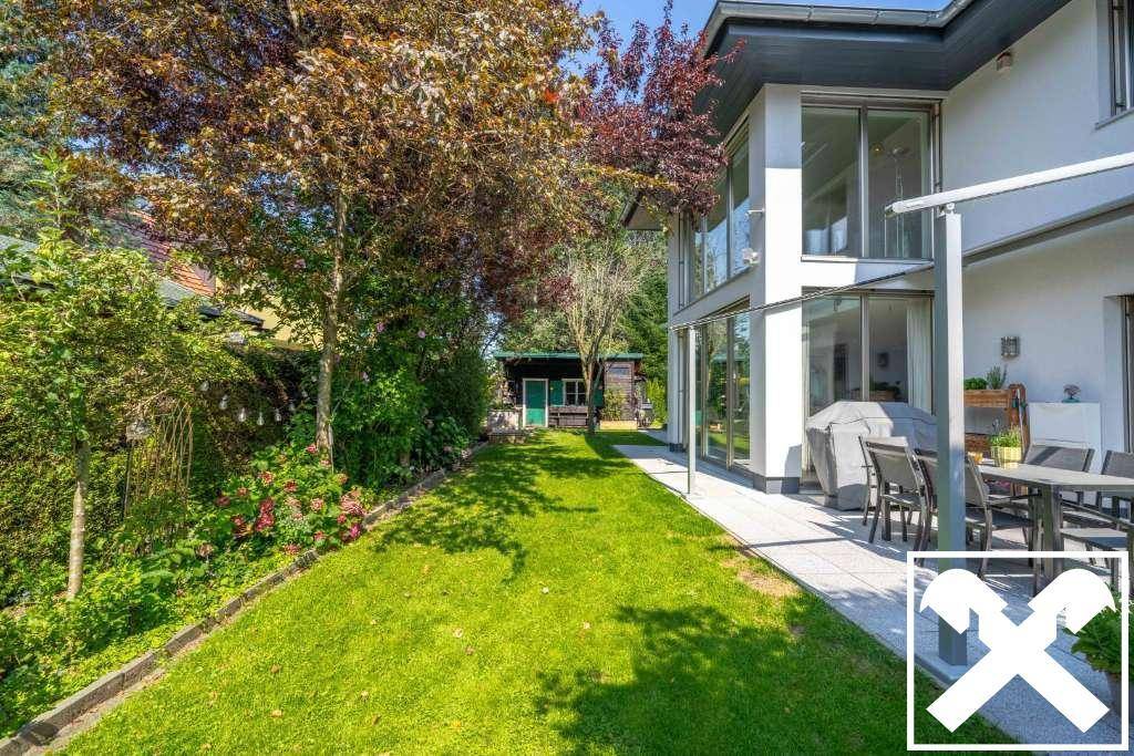 Gepflegter Garten mit Rasenfläche, Bäumen und einer Terrasse am Haus.