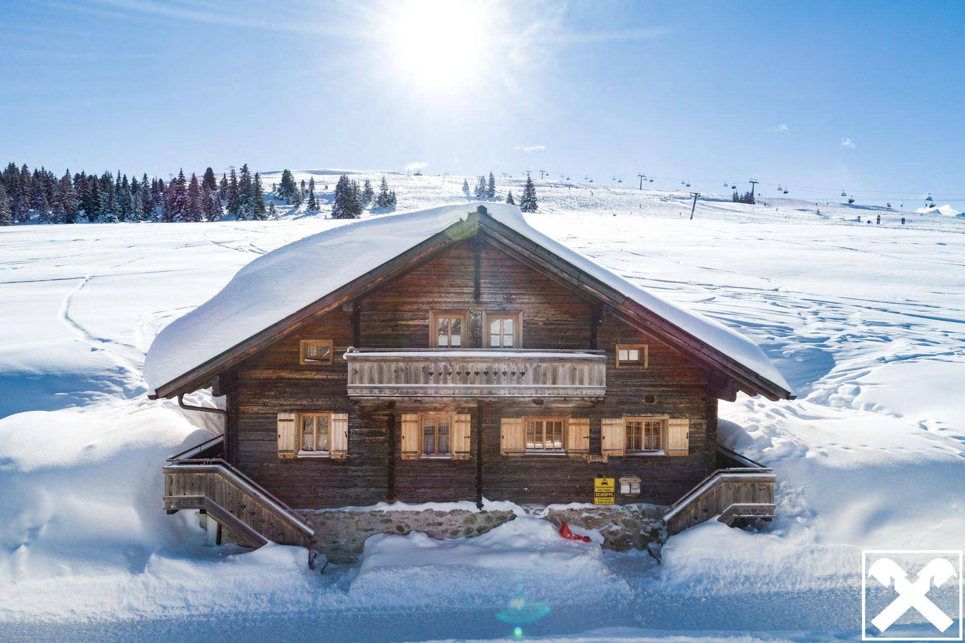 Idyllisches Holzchalet in einer tief verschneiten Winterlandschaft unter strahlend blauem Himmel.