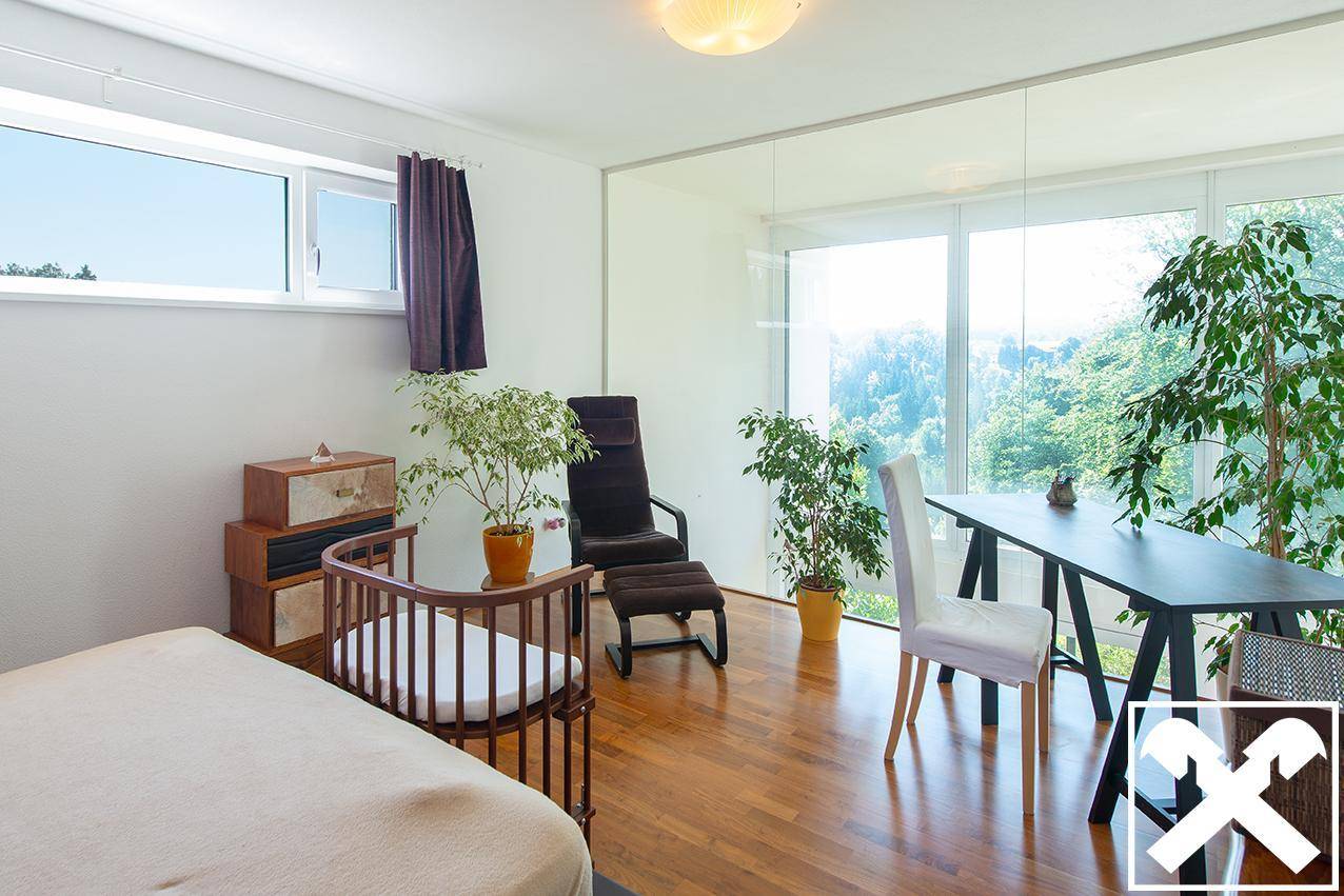 Helles Schlafzimmer mit Holzboden, großen Fenstern und Blick ins Grüne, ausgestattet mit einem Schreibtisch.