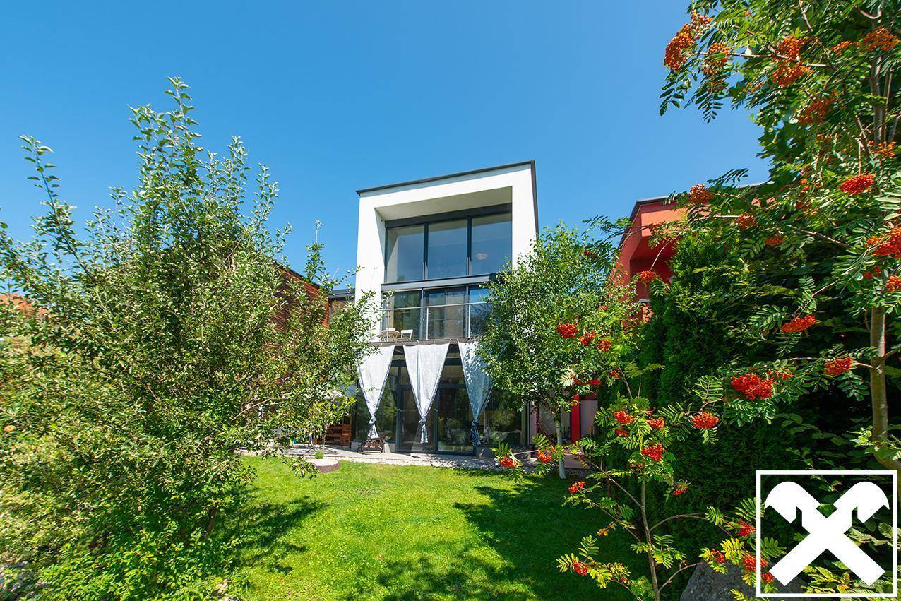 Moderner Neubau mit gepflegtem Garten, grüner Rasenfläche und blühenden Sträuchern.