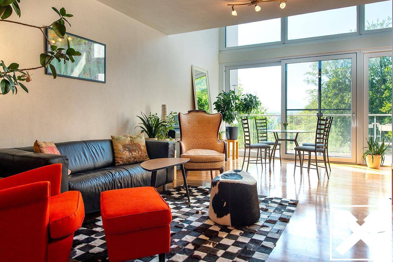 Gemütliches Wohnzimmer mit Ledersofa, farbigen Akzenten und großen Fenstern mit Zugang zum Balkon.