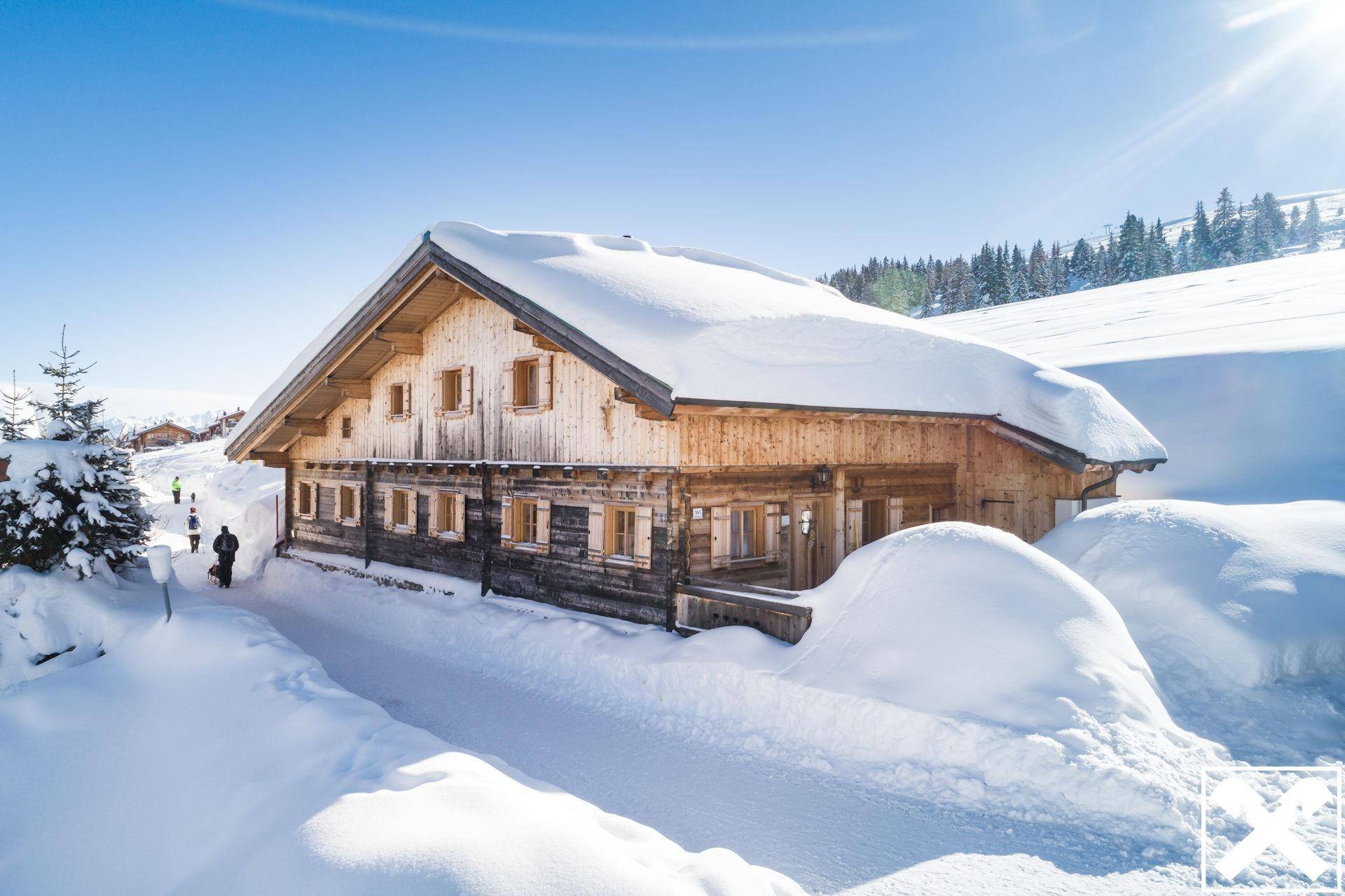 Traditionelles Holzchalet in verschneiter Berglandschaft unter blauem Himmel.