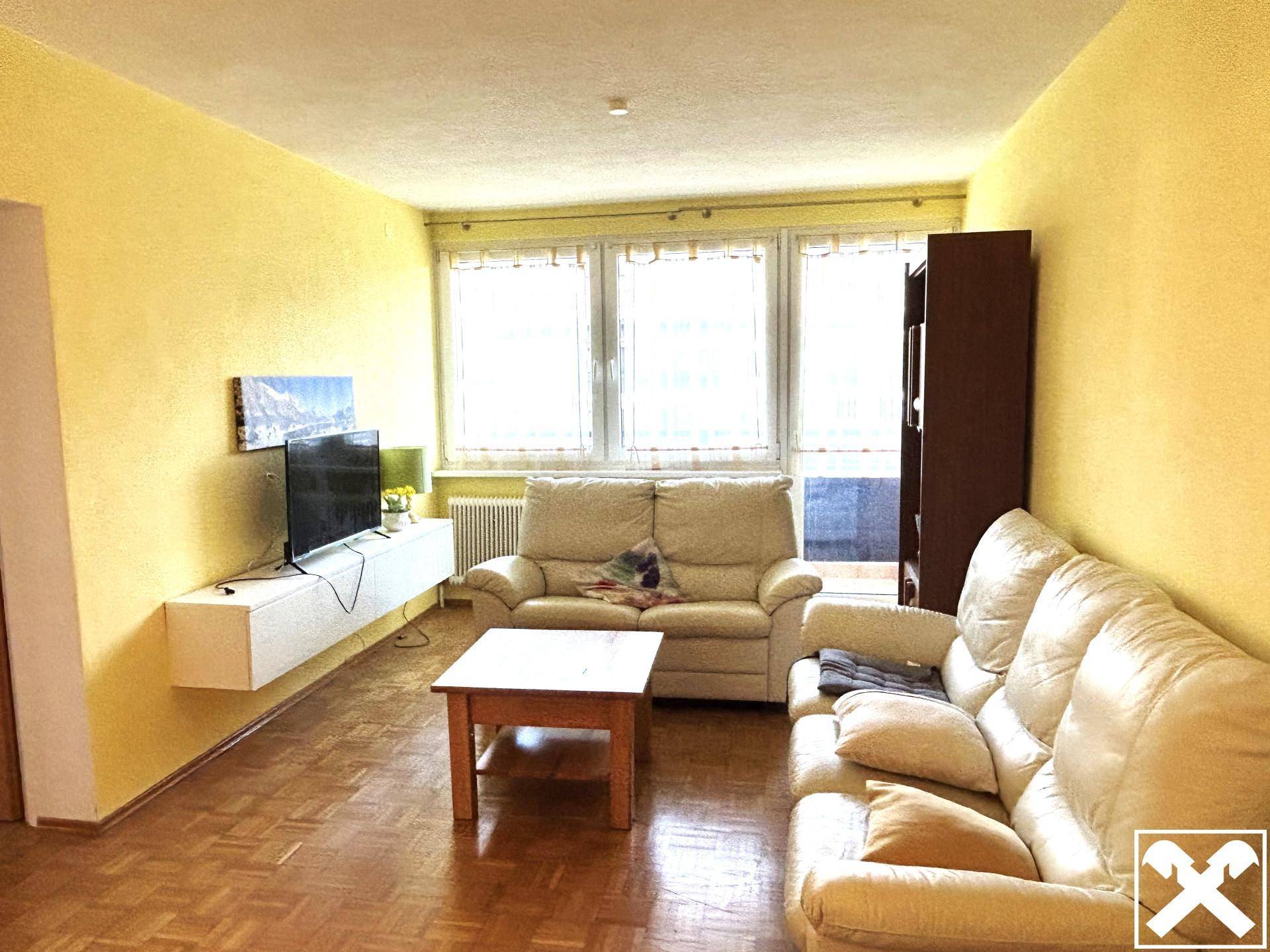 Gemütliches Wohnzimmer mit gelben Wänden, beigen Sofas, Parkettboden und Blick nach draußen.