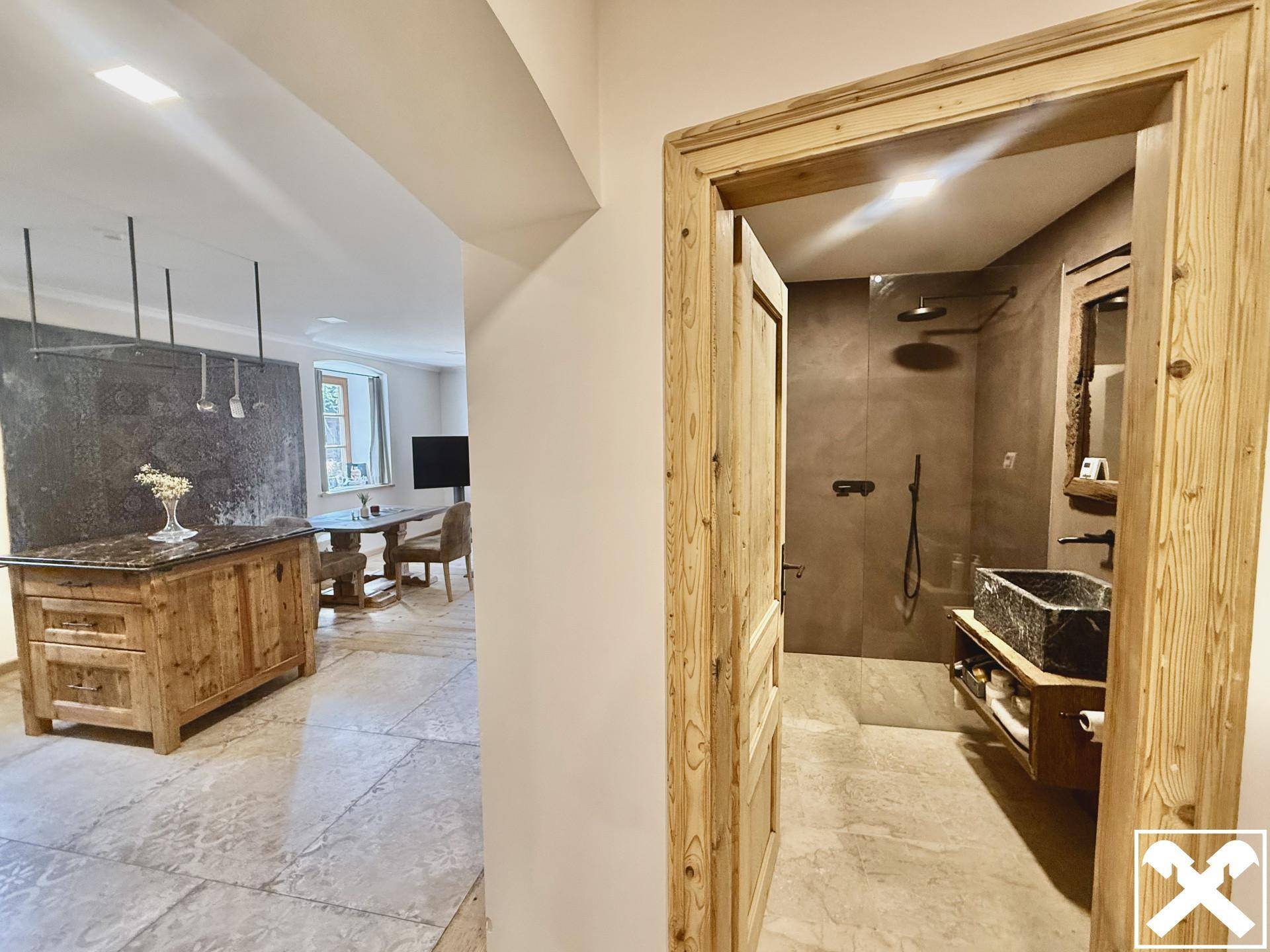 Flur mit Holztür und Blick in ein modernes Badezimmer, das eine begehbare Dusche zeigt.