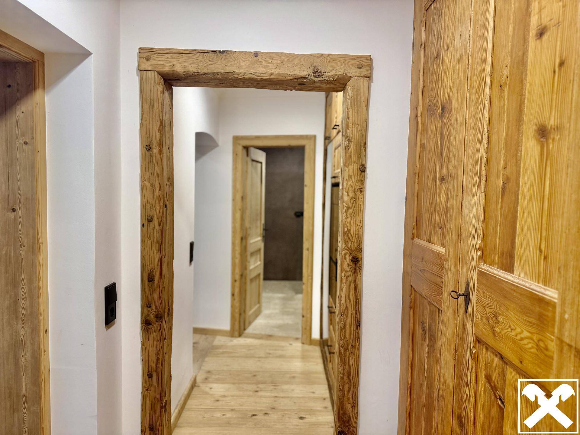 Heller Flur mit Holzböden und rustikalen Holztürrahmen, der zu weiteren Räumen führt.