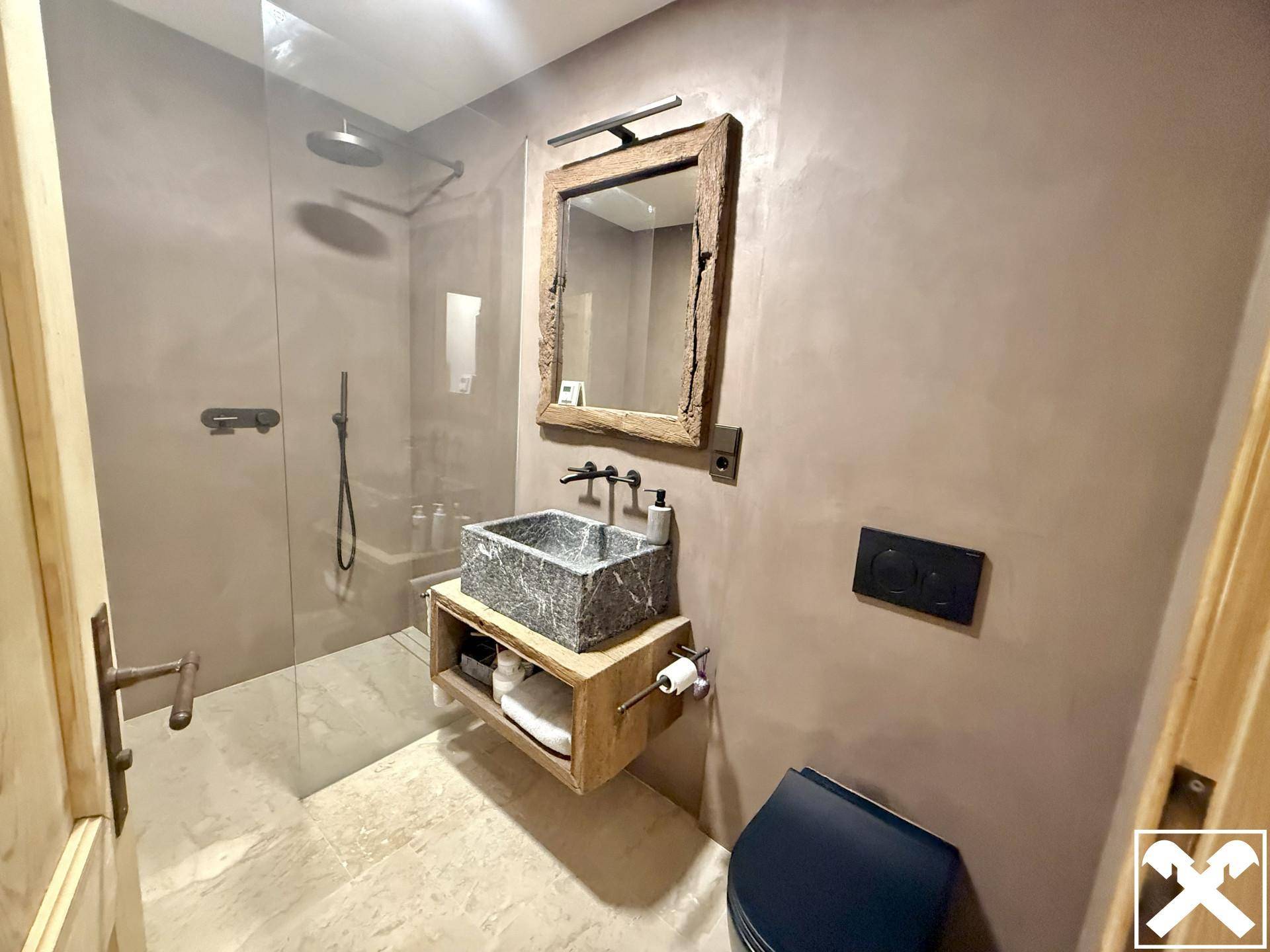 Modernes Badezimmer mit begehbarer Dusche, Steinwaschbecken und Wand-WC in neutralen Farbtönen.