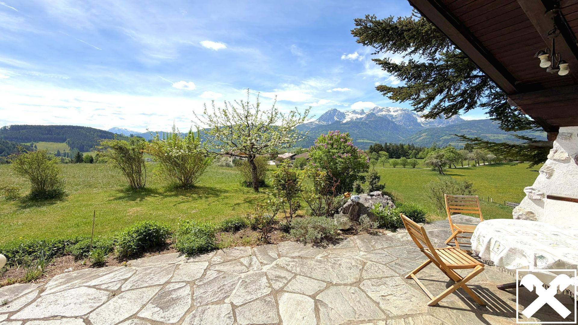 Steinplatten-Terrasse mit Gartenmöbeln und weitem Blick auf die umliegende Berglandschaft.