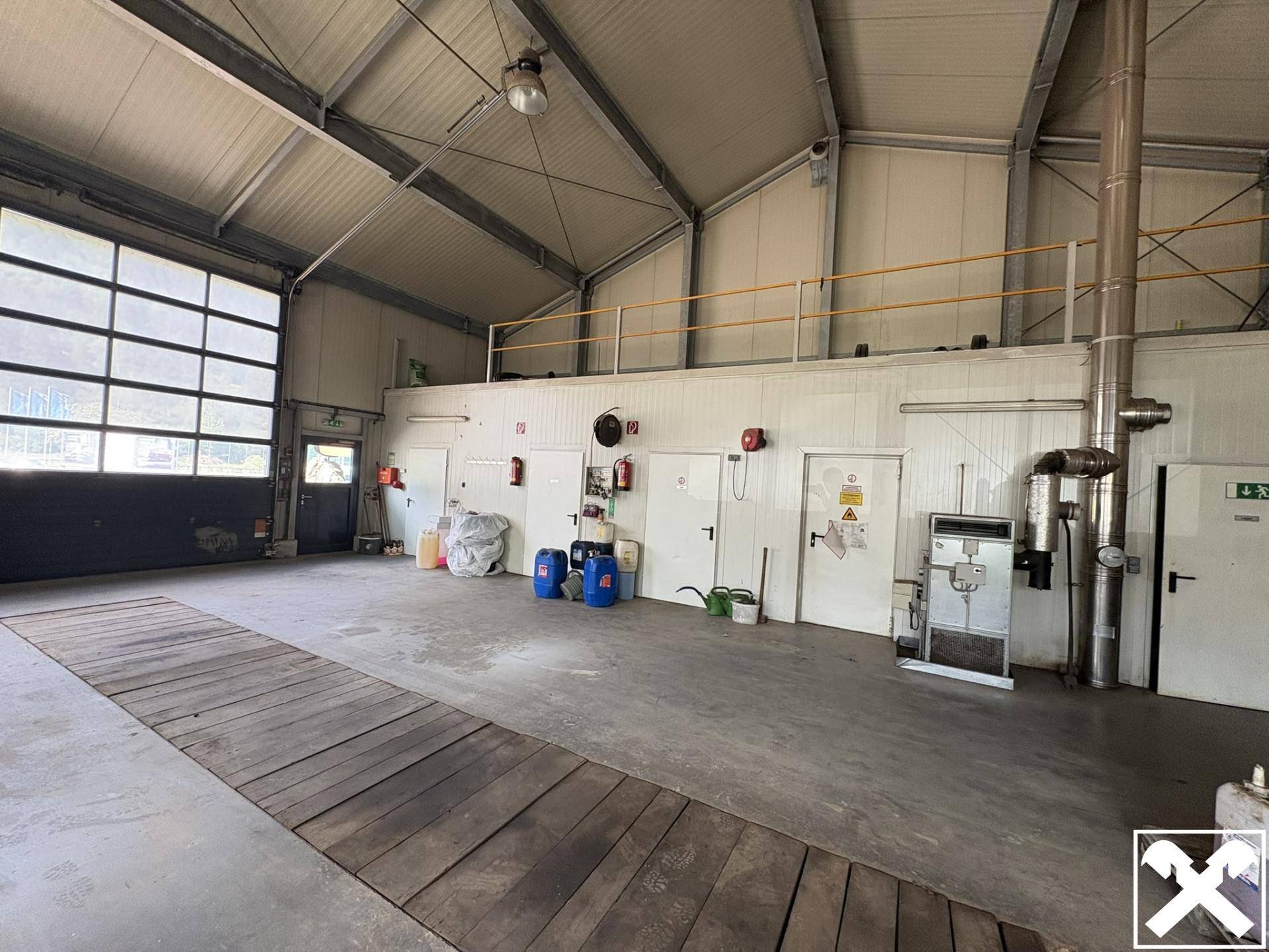 Geräumige Industriehalle mit hohen Decken, Betonboden und einem großen Sektionaltor, ideal für gewerbliche Nutzung.