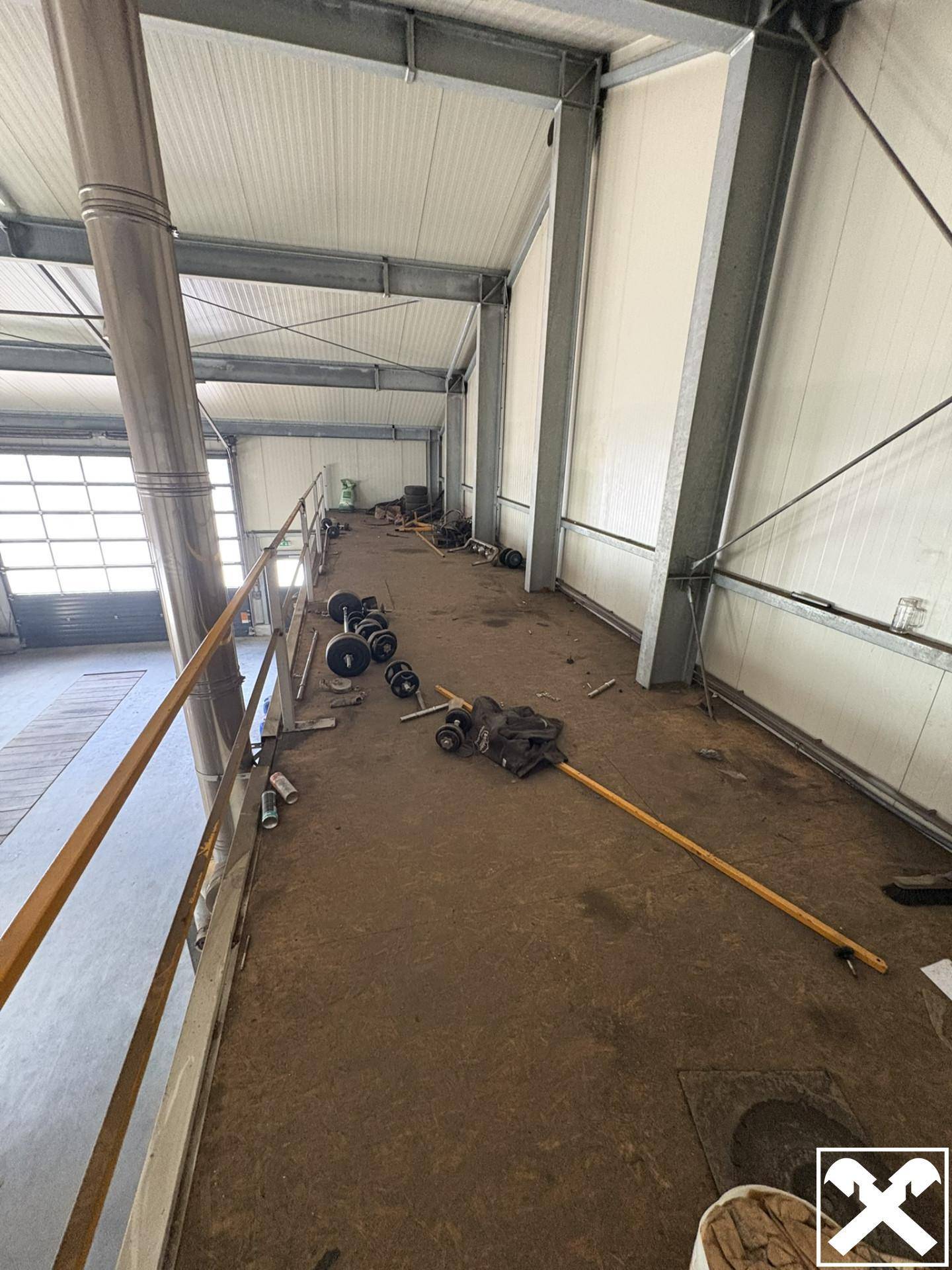 Blick auf die erhöhte Zwischenebene der Industriehalle mit Geländer und einigen Fitnessgeräten, die als Lagerfläche dient.