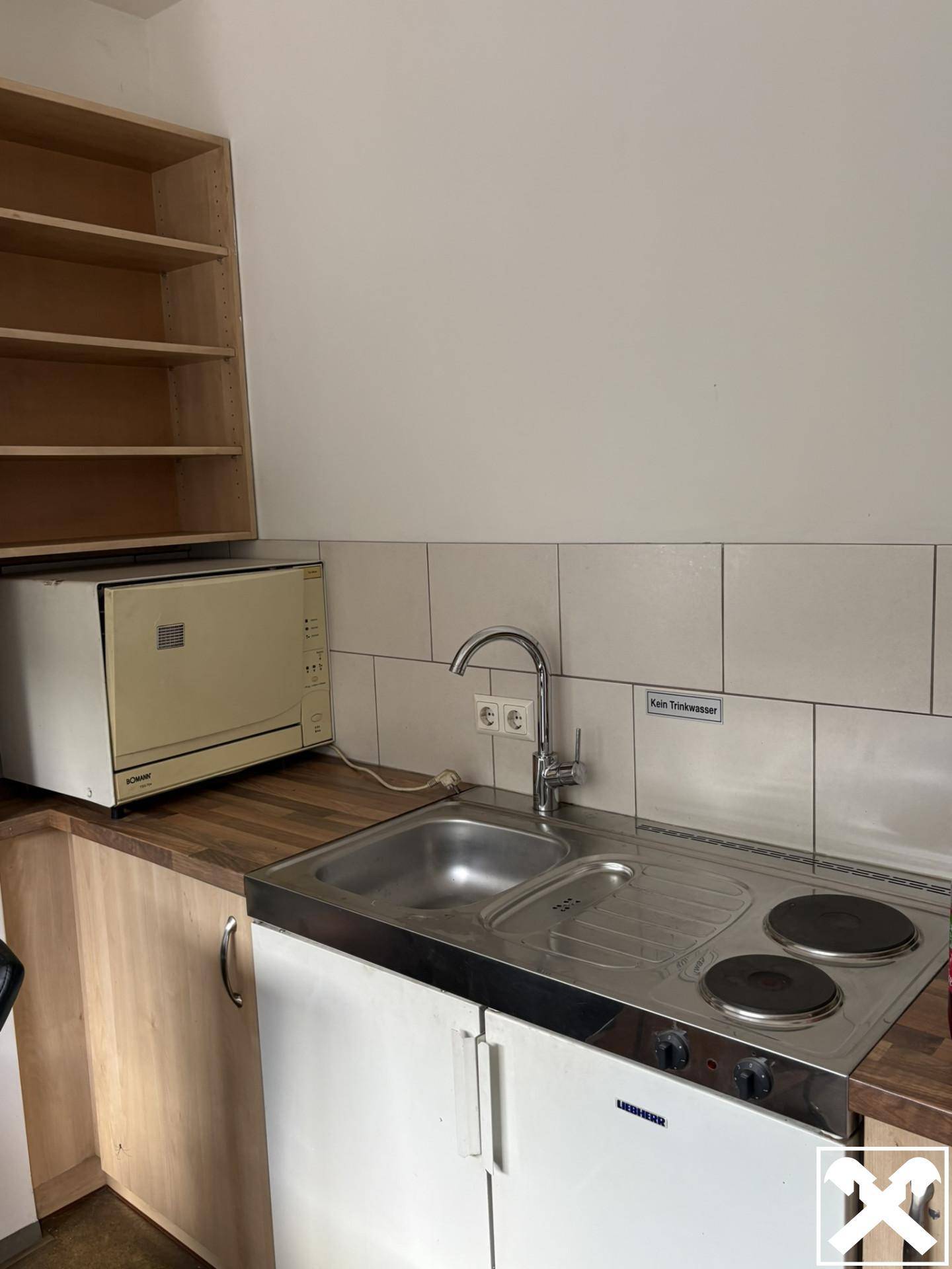 Kleine Küchenzeile mit Spüle, zwei Kochplatten und Mikrowelle, ideal für eine schnelle Zubereitung von Mahlzeiten.