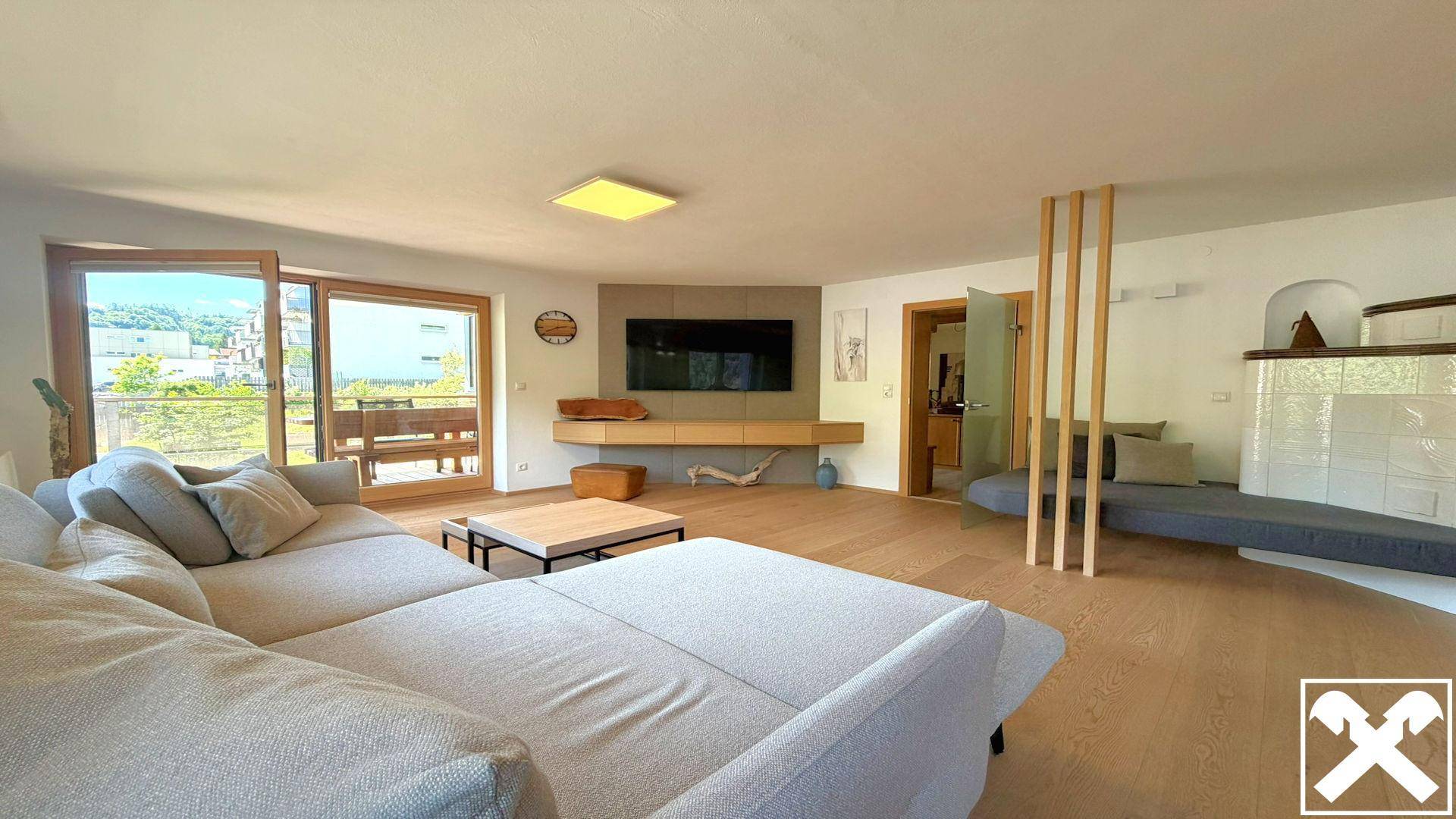Helles Wohnzimmer mit großem Sofa, Holzboden und Zugang zu einem Außenbereich mit Bergblick.