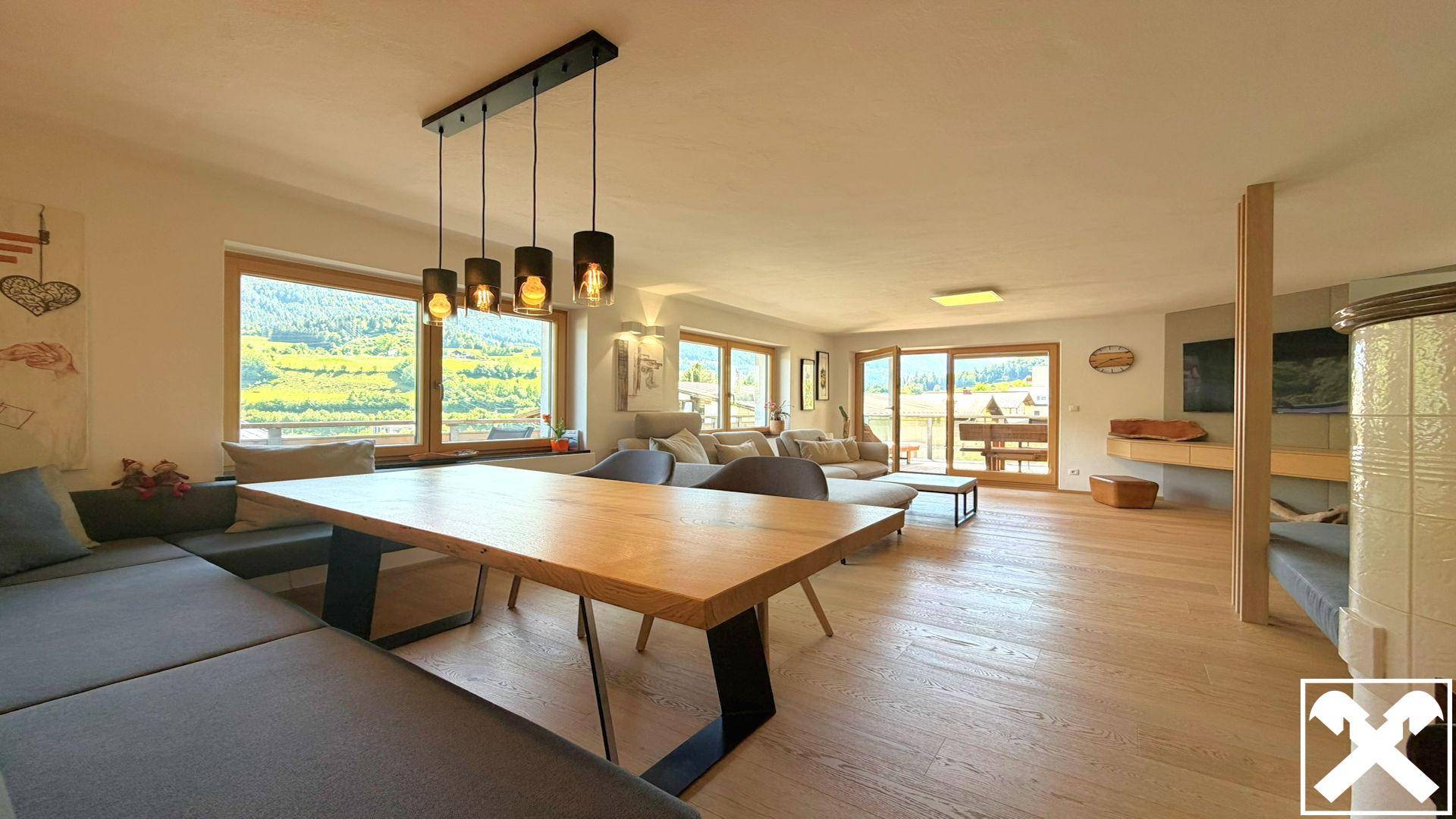 Geräumiger Wohn-Essbereich mit Holzboden, großem Esstisch und Zugang zu einem Balkon mit Bergblick.