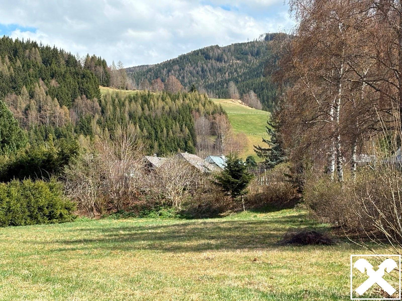 Panoramablick auf bewaldete Berge und grüne Hügel mit einigen Häusern in der Ferne.