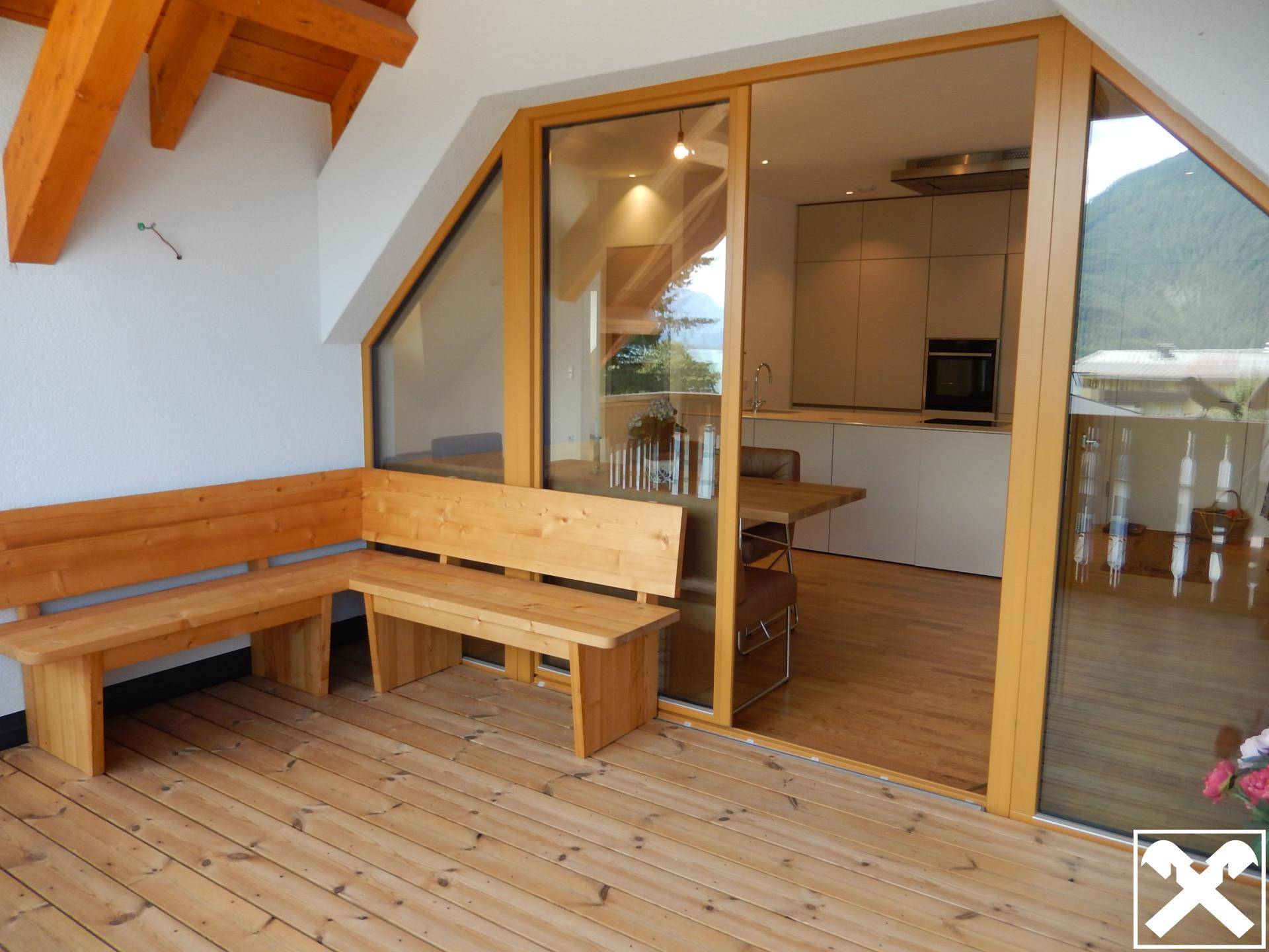Geräumiger Balkon mit Holzbänken und Zugang zum offenen Wohnbereich mit Seeblick.