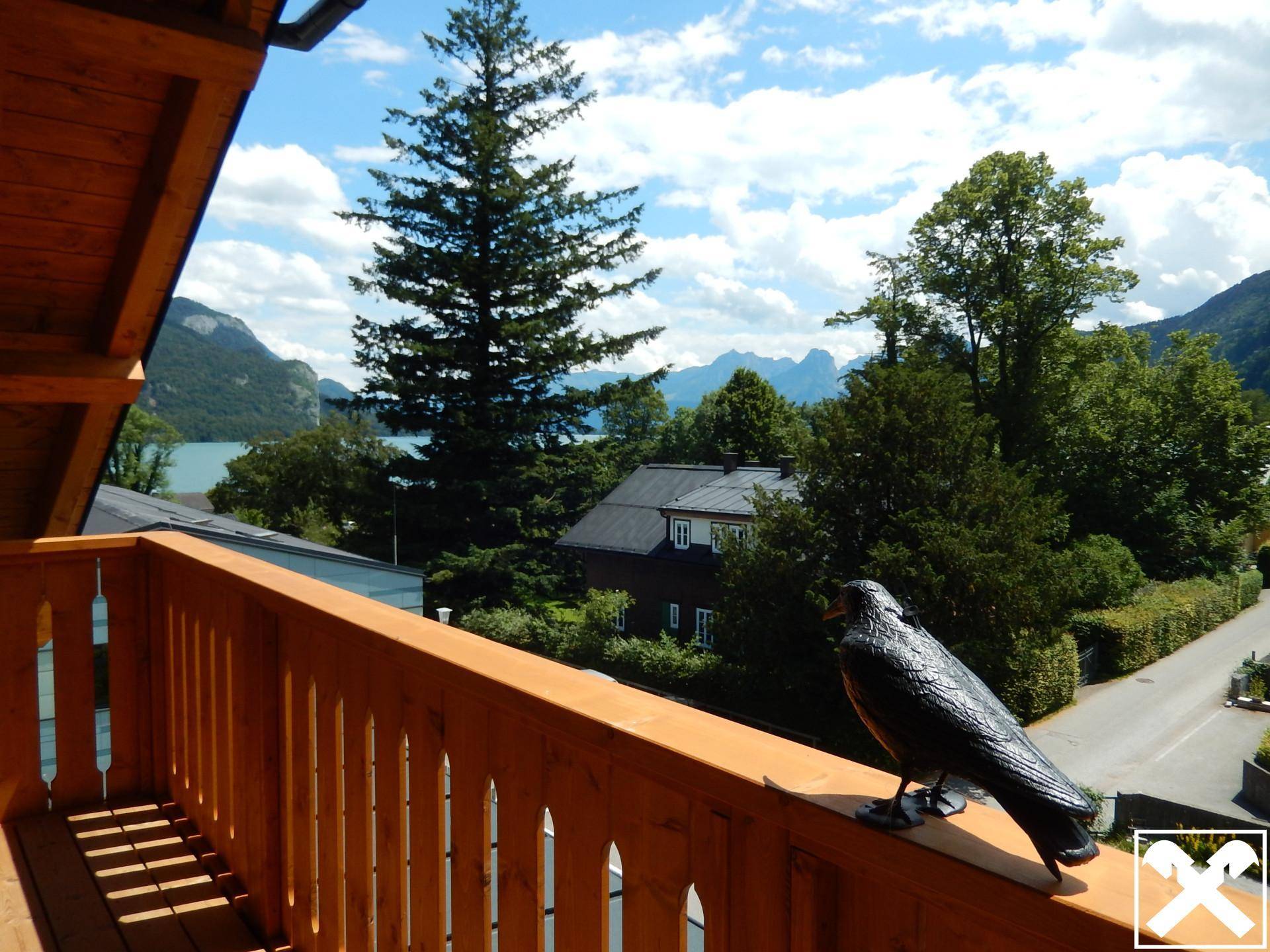 Balkon mit traditionellem Holzgeländer und weitem Blick über die Dächer zum See und den Bergen.