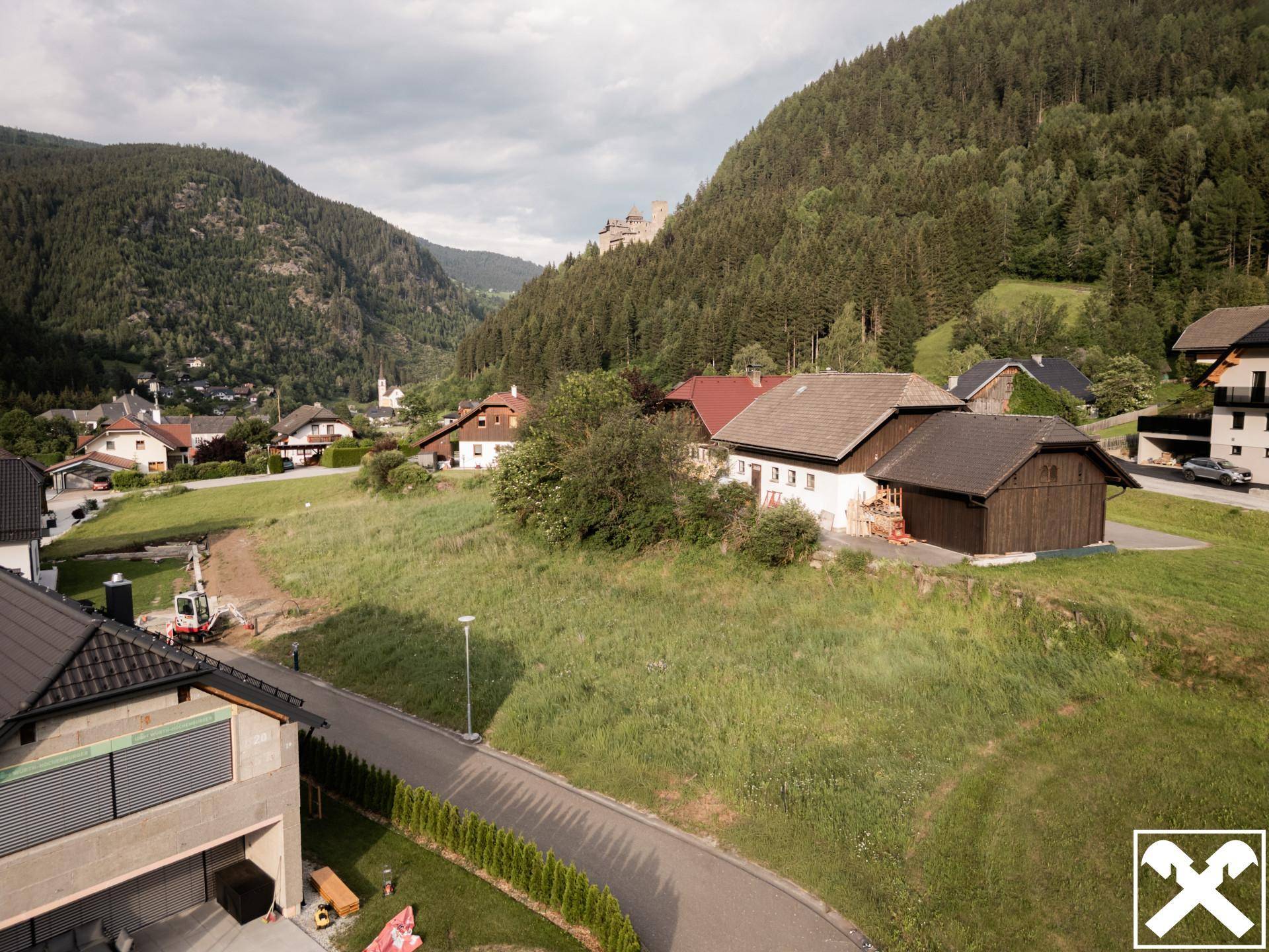 Panoramablick auf die ländliche Siedlung umgeben von grünen Hügeln und Bergen unter bewölktem Himmel.