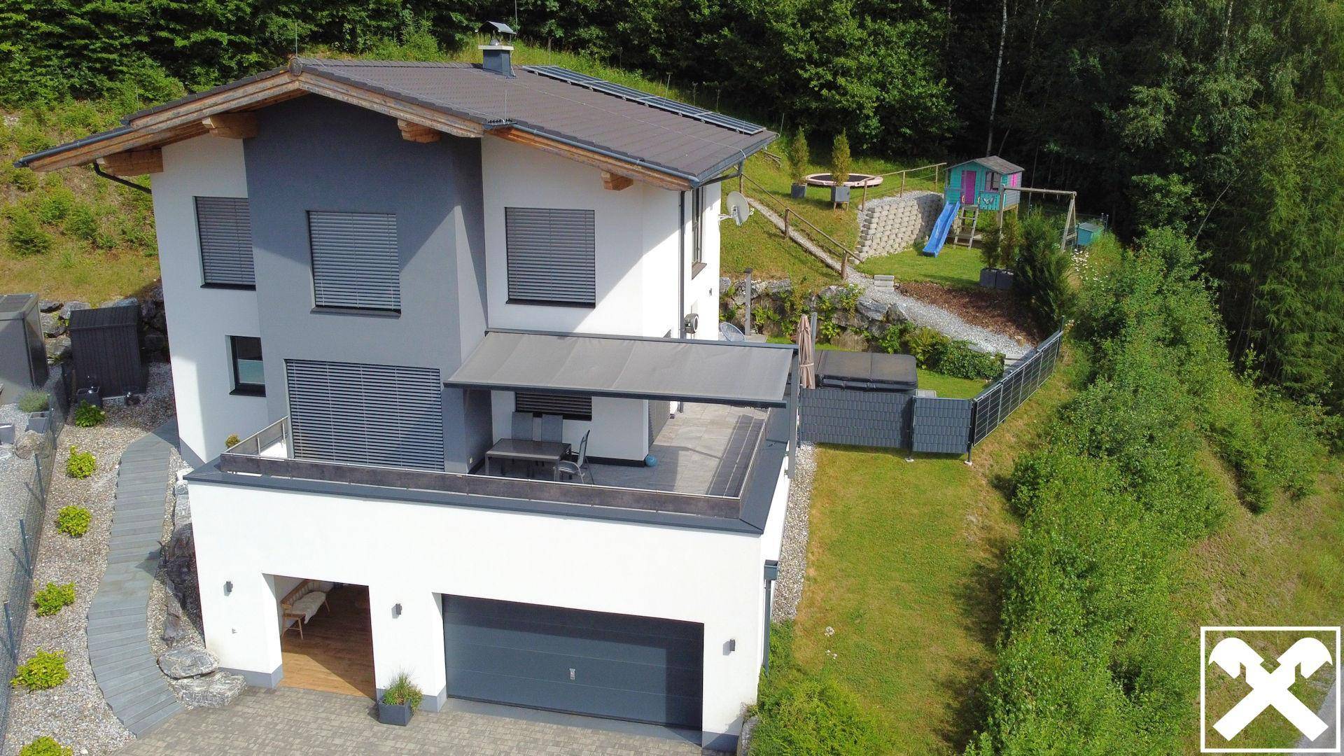 Moderne Villa mit großer Terrasse, Gartenmöbeln und Spielplatz im Grünen.