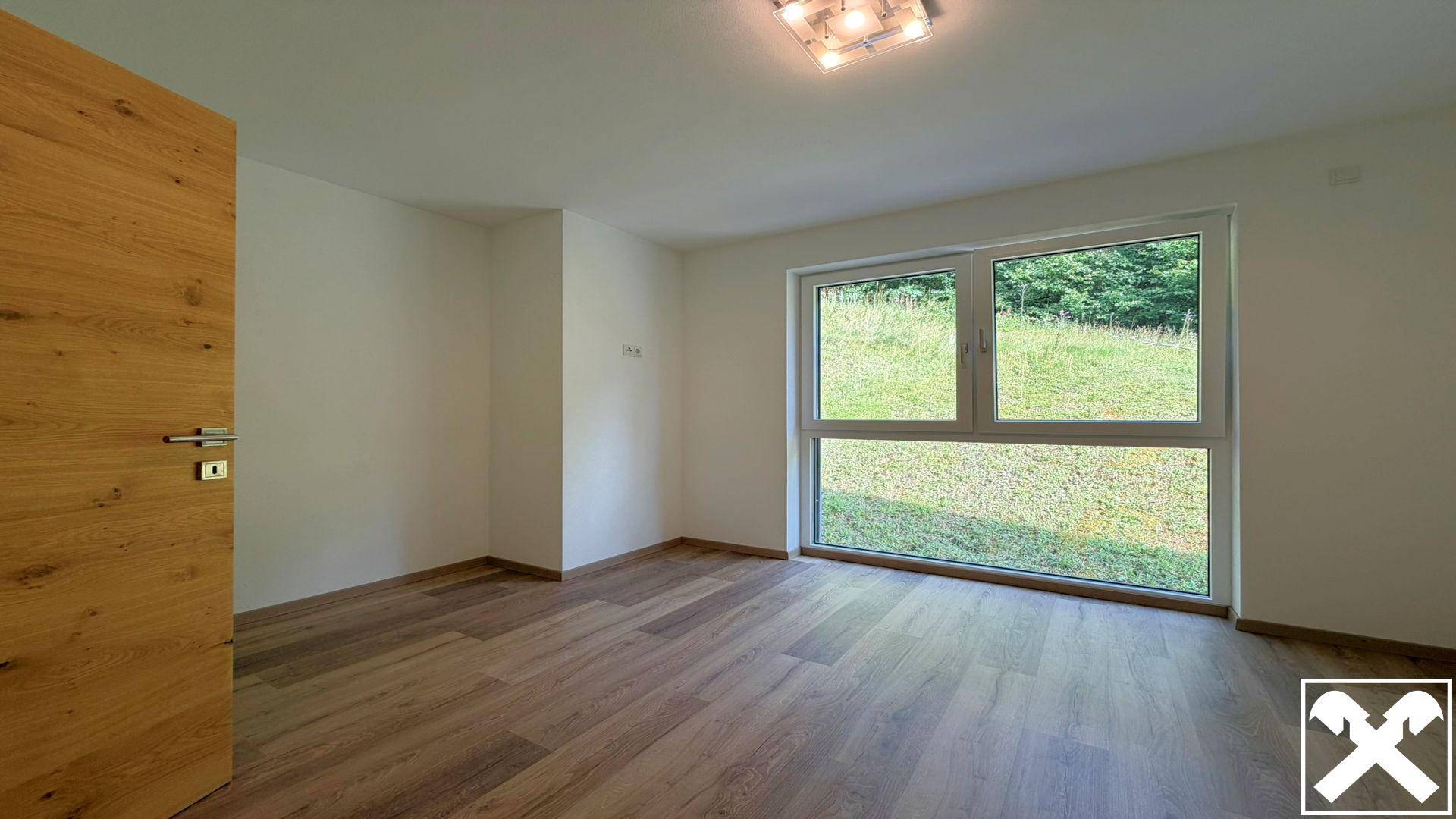 Helles Schlafzimmer mit Holzboden und großem Fenster mit Blick ins Grüne.
