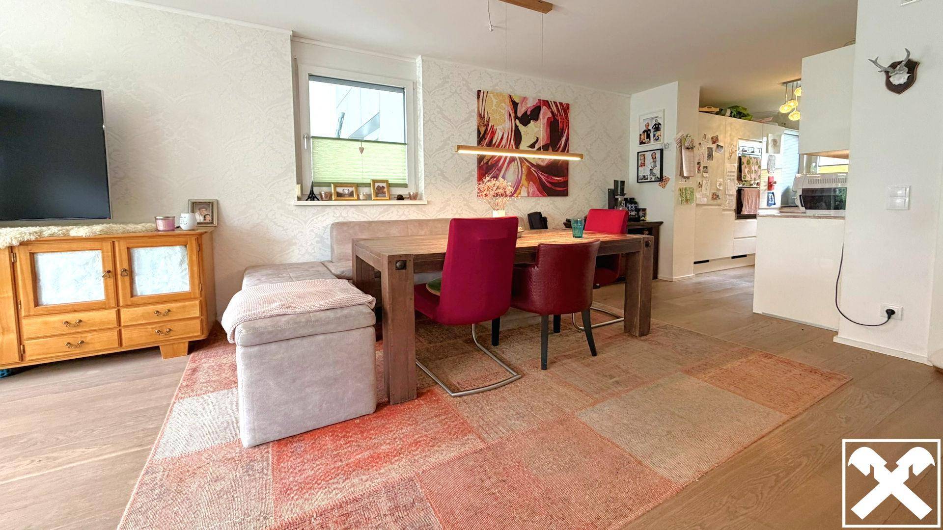 Offener Wohn- und Essbereich mit Holztisch, farbigen Stühlen und Blick in die Küche.