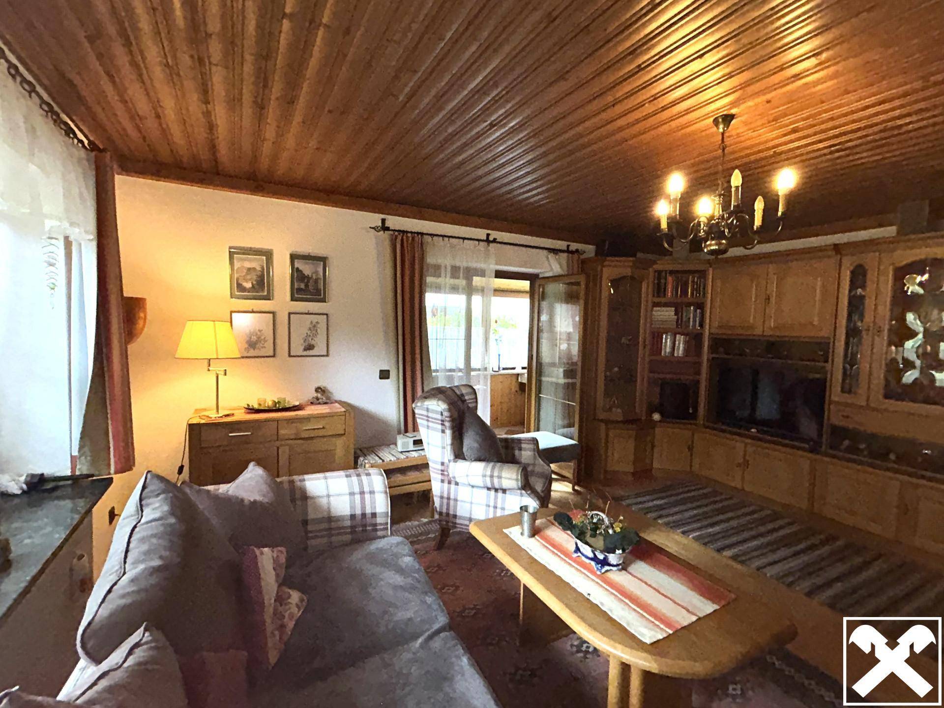 Gemütliches Wohnzimmer im Alpenstil mit Holzdecke, traditionellen Möbeln und Balkonzugang.