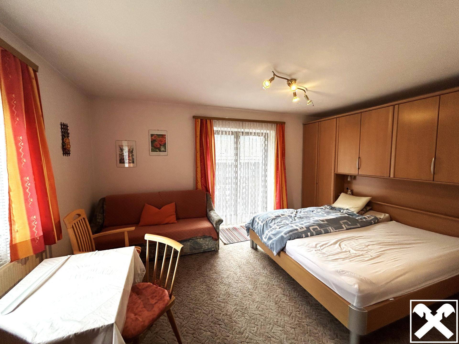 Schlafzimmer mit Doppelbett, Sofa, Esstisch und praktischen Einbauschränken.