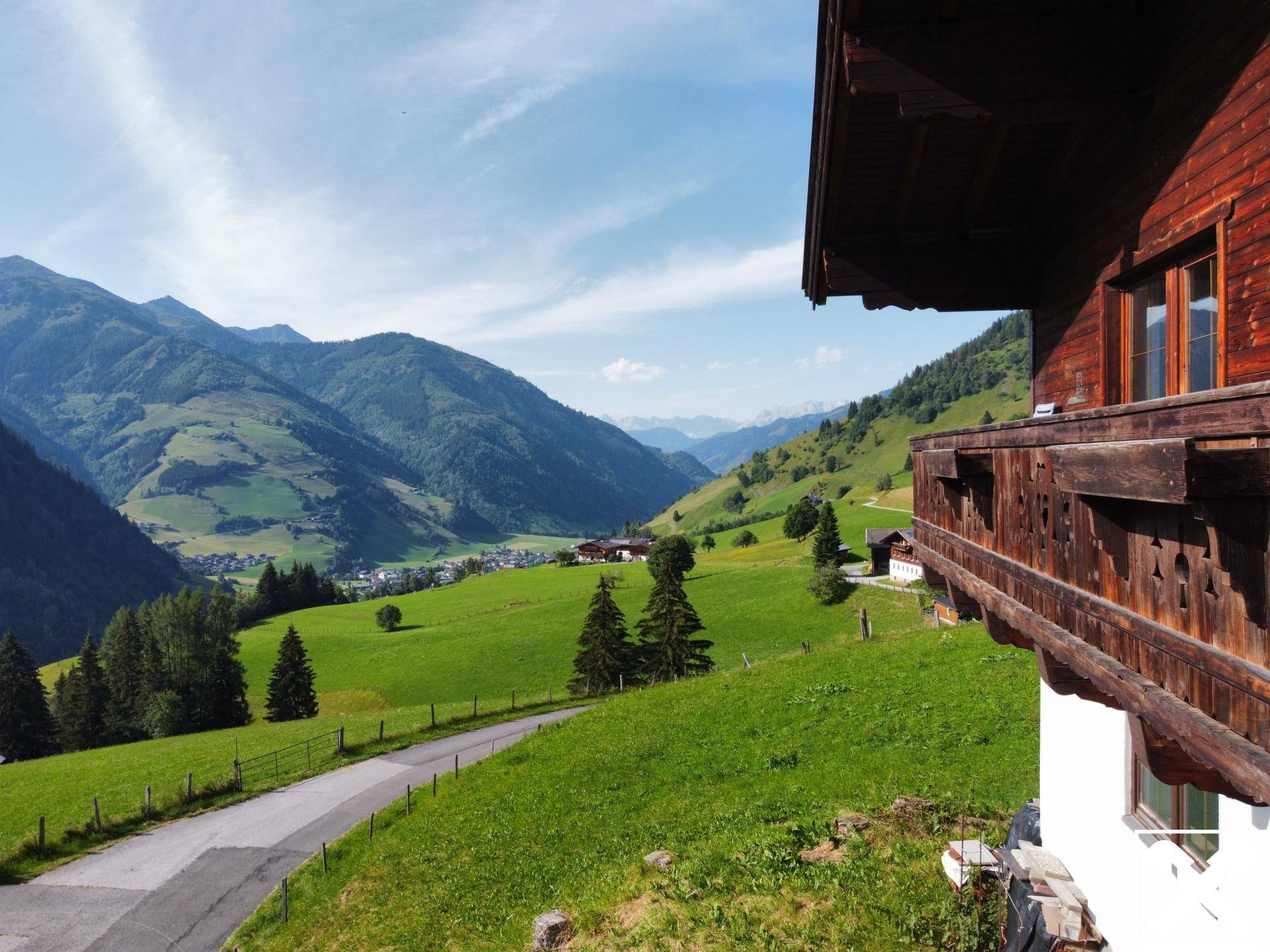 Panoramablick vom Holzbalkon über ein grünes Tal mit majestätischen Bergen im Hintergrund.