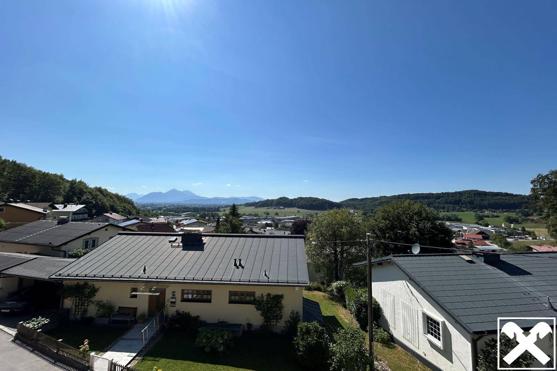 Weitläufiger Panoramablick über die umliegende Landschaft mit Bergen und Siedlung bei strahlendem Sonnenschein.