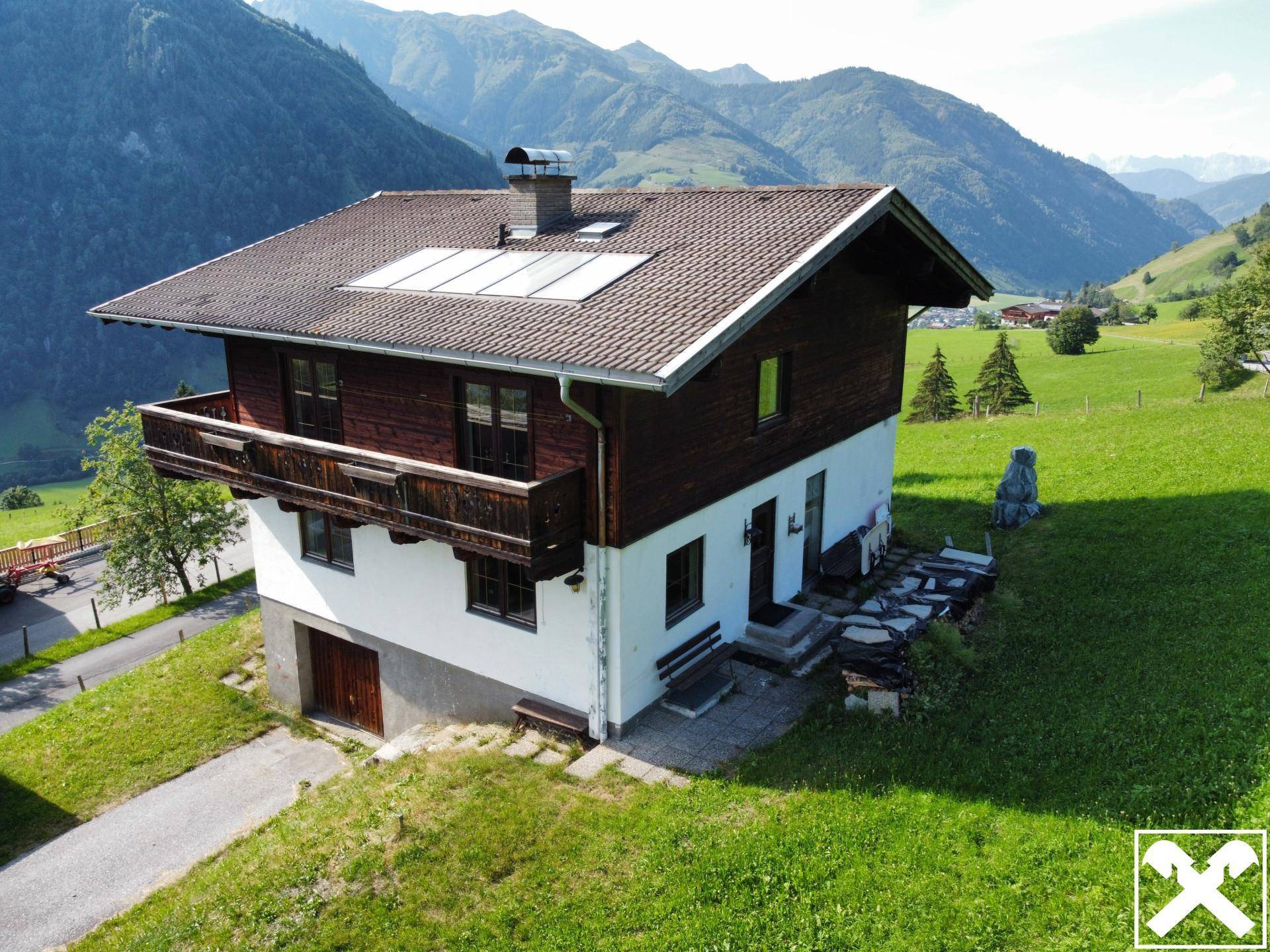 Traditionelles Haus mit Photovoltaikanlage auf dem Satteldach, eingebettet in eine grüne Berglandschaft.