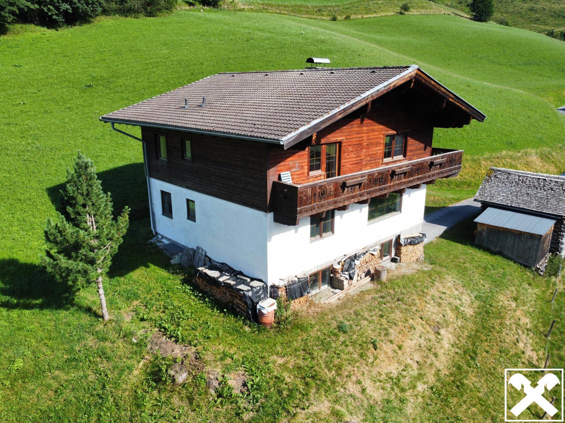 Charmantes Landhaus im Grünen mit Holzfassade und gestapeltem Brennholz am Fundament.